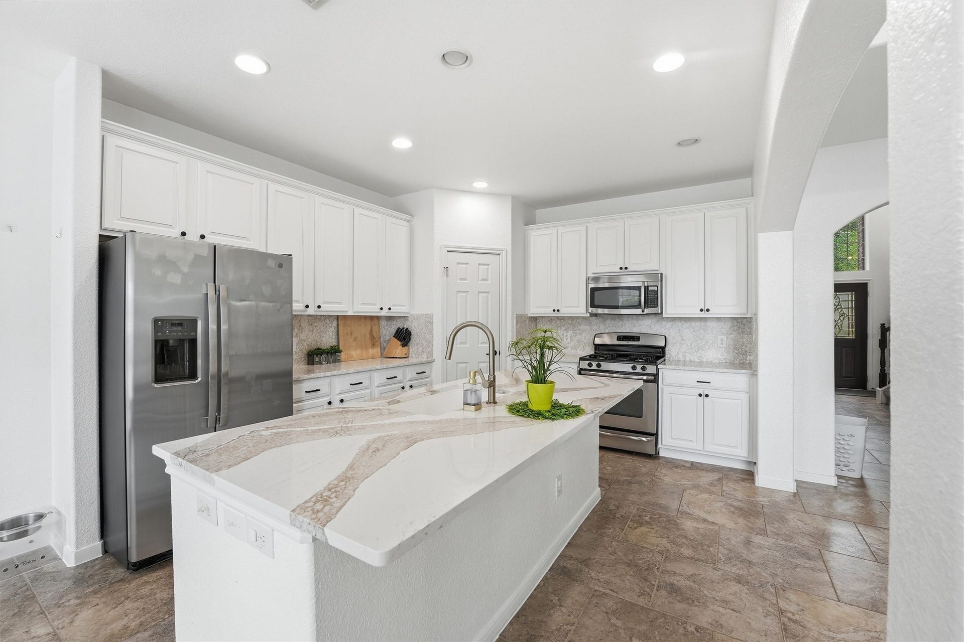 This spacious living room features high ceilings, a cozy fireplace, and a modern design. It includes a comfortable seating area, a wall-mounted TV, and stylish lighting. The room opens up to a second-floor balcony and is adjacent to a welcoming entryway with natural light.