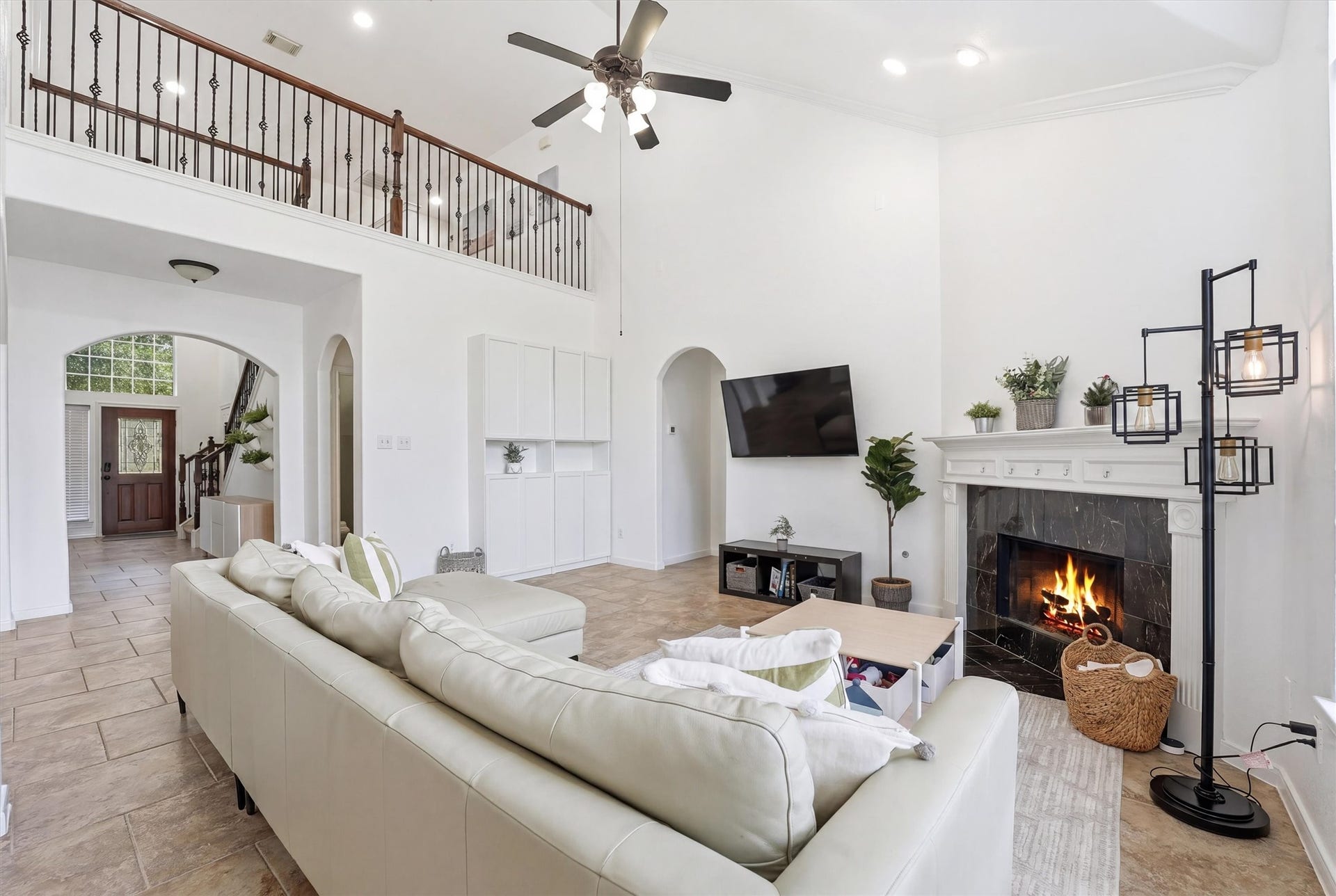 This inviting living space features high vaulted ceilings and abundant natural light. It includes a cozy fireplace, a spacious sectional sofa, and an open layout leading to a modern kitchen. Ideal for comfort and entertaining.