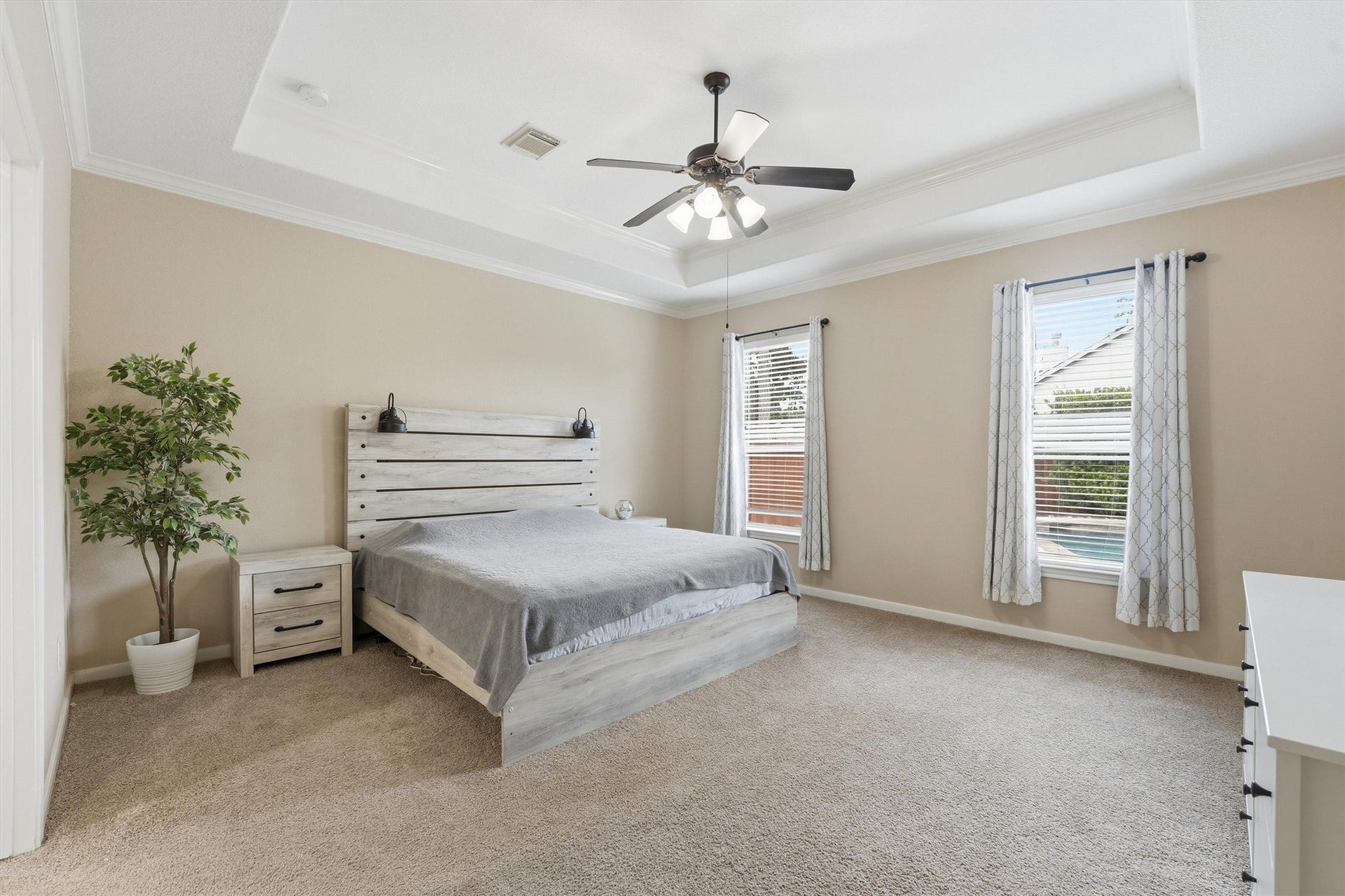 This photo showcases a bright, carpeted upstairs hallway with a decorative wrought iron railing overlooking a staircase. It features double doors with glass accents and a wall-mounted beach-themed artwork, creating a relaxed and inviting atmosphere.