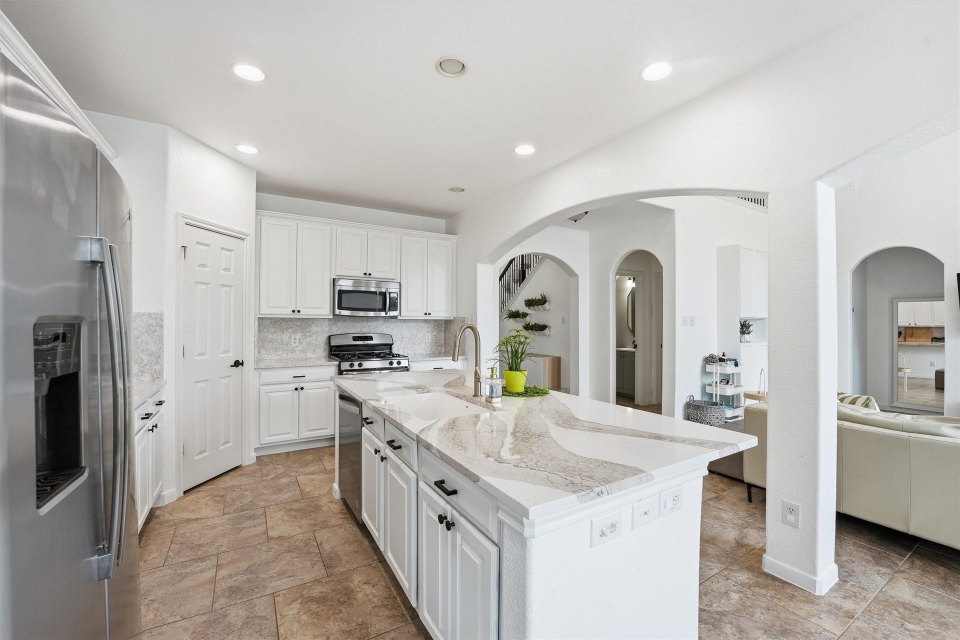 Bright and modern kitchen with sleek white cabinetry, stainless steel appliances, and a large island with a marble countertop. The space features recessed lighting and a tile floor, creating an inviting atmosphere.