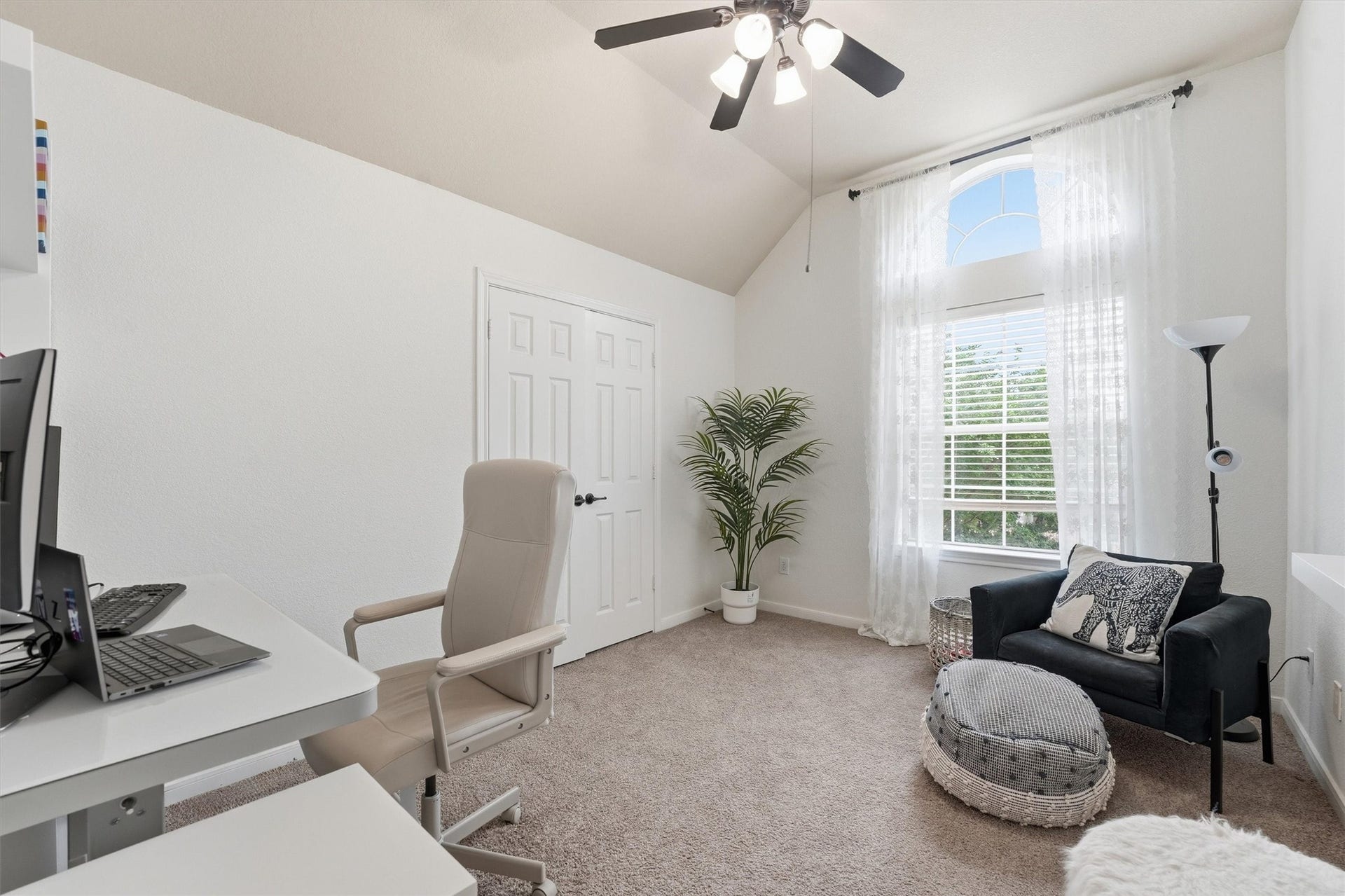 This cozy bedroom features soft blue walls, a large arched window with white curtains, and carpeted flooring. It's decorated with playful fire truck accents and includes a comfortable bed, making it ideal for a child's room.