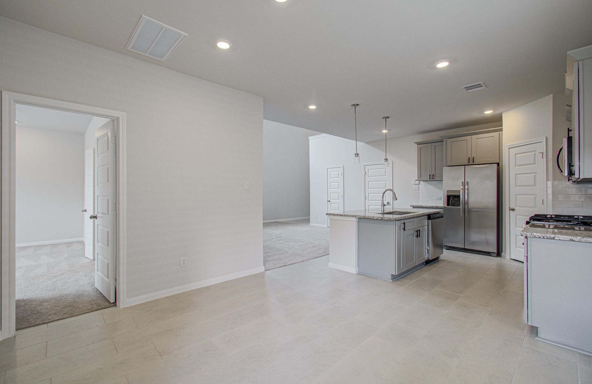 14210 Aston Pine Drive, Houston, TX 77032 Modern open-concept kitchen with sleek stainless steel appliances, granite countertops, and stylish pendant lighting, seamlessly flowing into a spacious living area and adjacent room. Please Note this is a different home/floorplan in the community.
