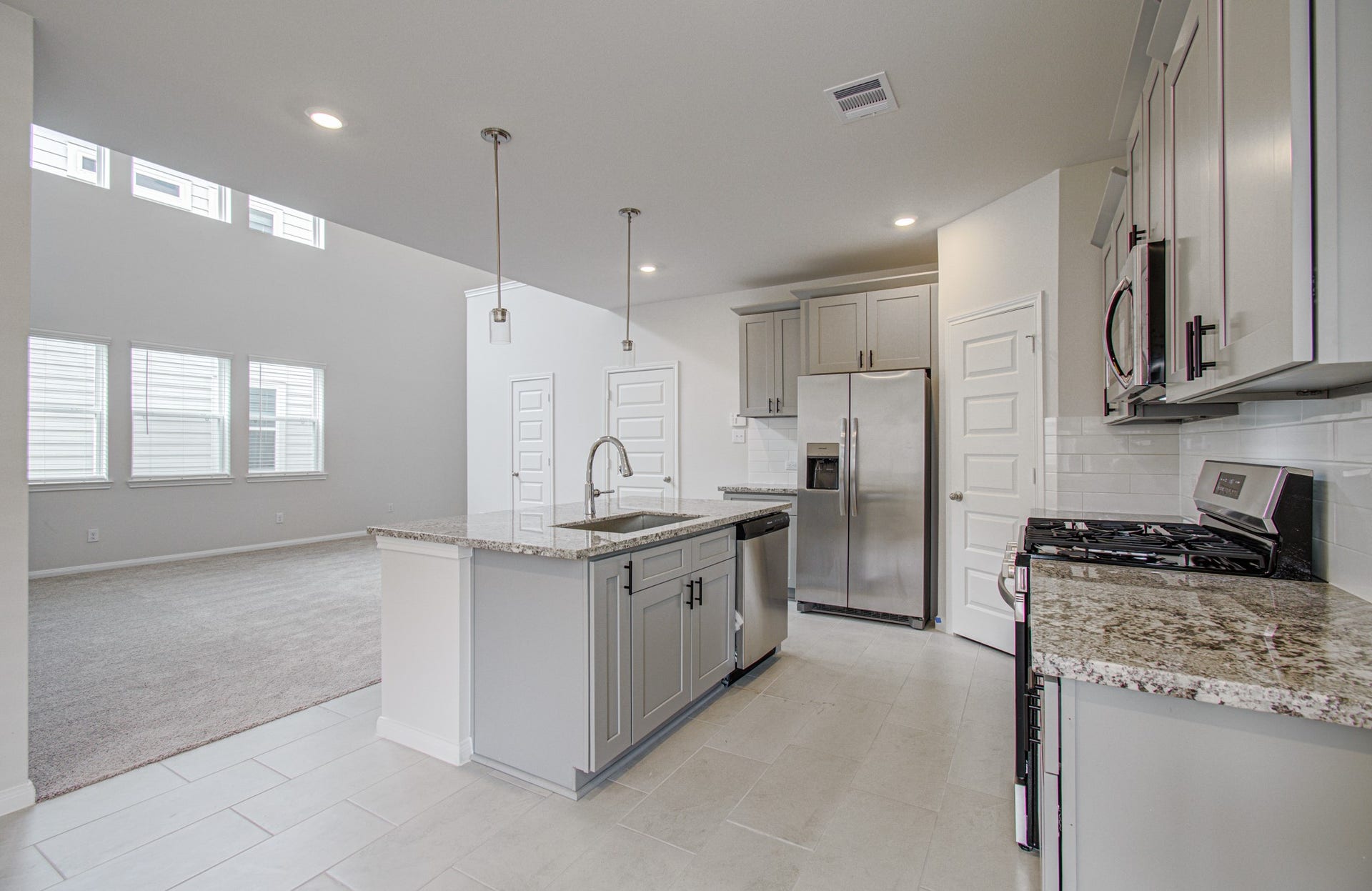 14210 Aston Pine Drive, Houston, TX 77032 Modern kitchen with granite countertops, stainless steel appliances, and ample cabinetry, seamlessly flowing into a bright, open living area with large windows. Please Note this is a different home/floorplan in the community.