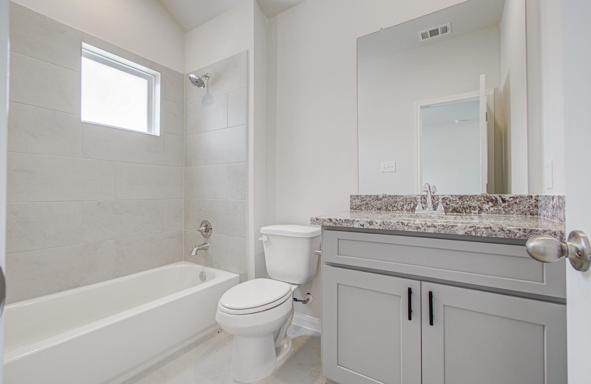 14210 Aston Pine Drive, Houston, TX 77032 Modern secondary bathroom featuring a sleek granite countertop, elegant gray cabinetry, and a spacious bathtub with stylish tile surround. Please Note this is a different home/floorplan in the community.