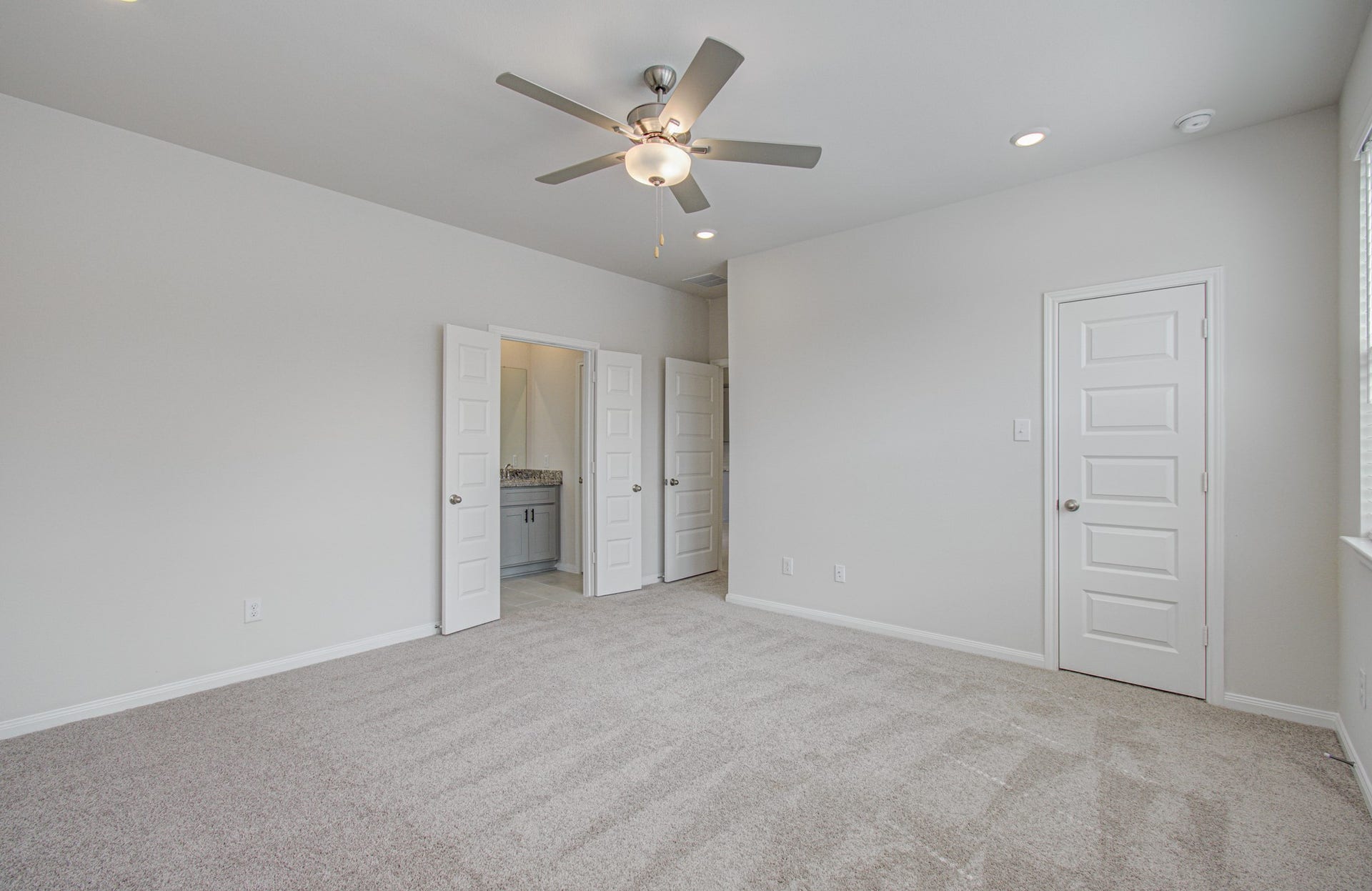 14210 Aston Pine Drive, Houston, TX 77032 Spacious primary bedroom with plush carpeting, neutral tones, a ceiling fan, and convenient en-suite bathroom access. Please Note this is a different home/floorplan in the community.