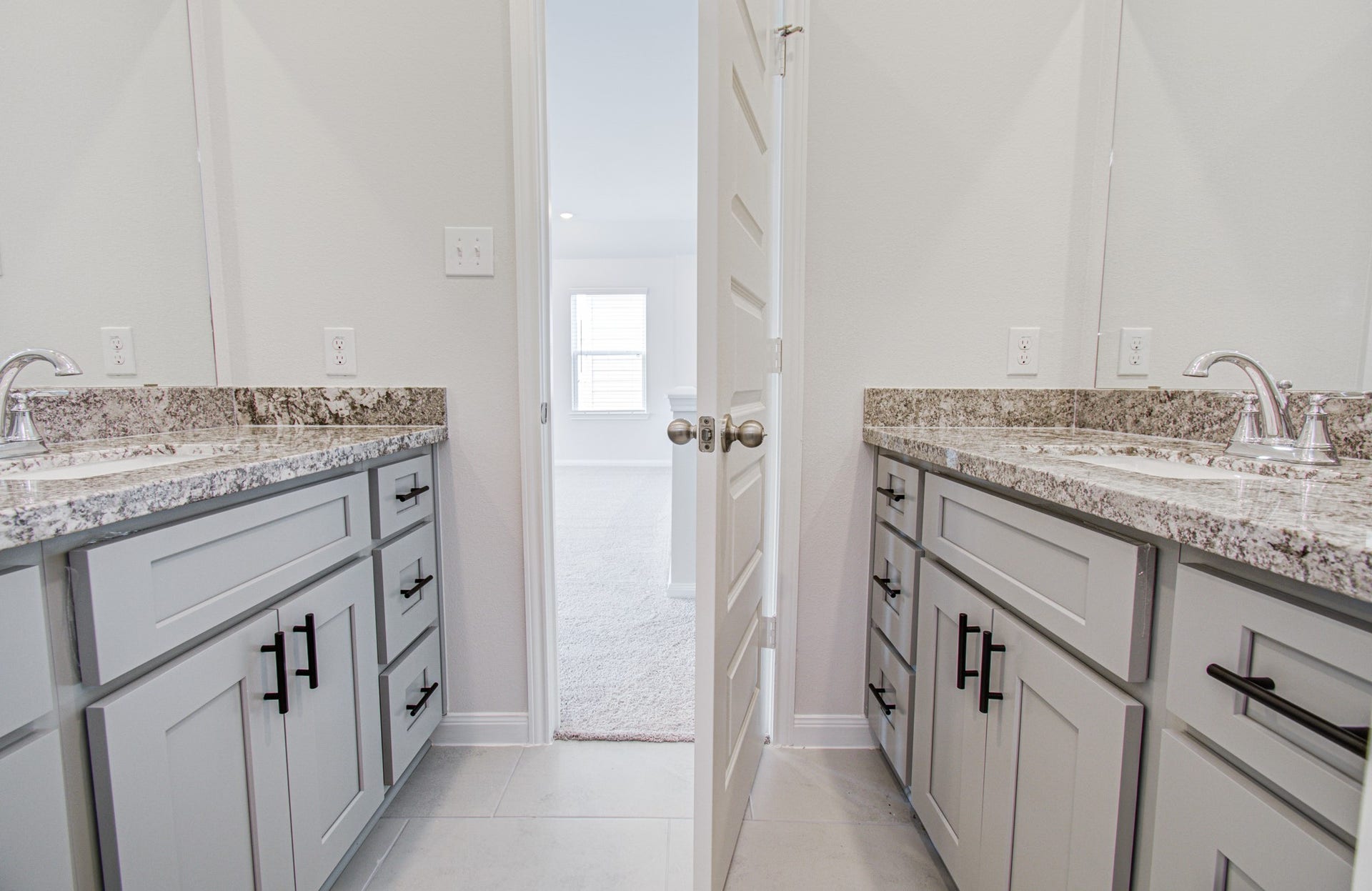 14210 Aston Pine Drive, Houston, TX 77032 Elegant dual vanity third bathroom with granite countertops and sleek cabinetry, leading into a bright, inviting room. Please Note this is a different home/floorplan in the community.