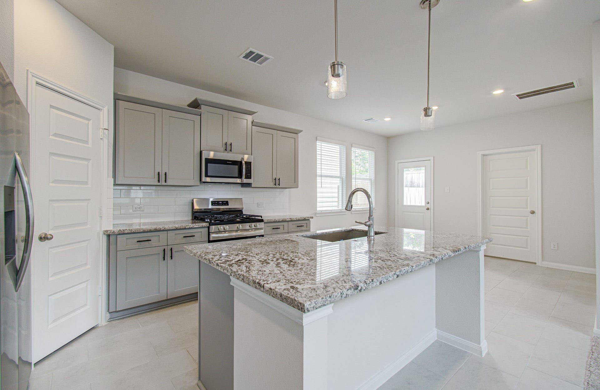 14210 Aston Pine Drive, Houston, TX 77032 Modern kitchen with sleek granite countertops, stainless steel appliances, and stylish gray cabinetry, offering ample natural light and a functional open layout. Please Note this is a different home/floorplan in the community.