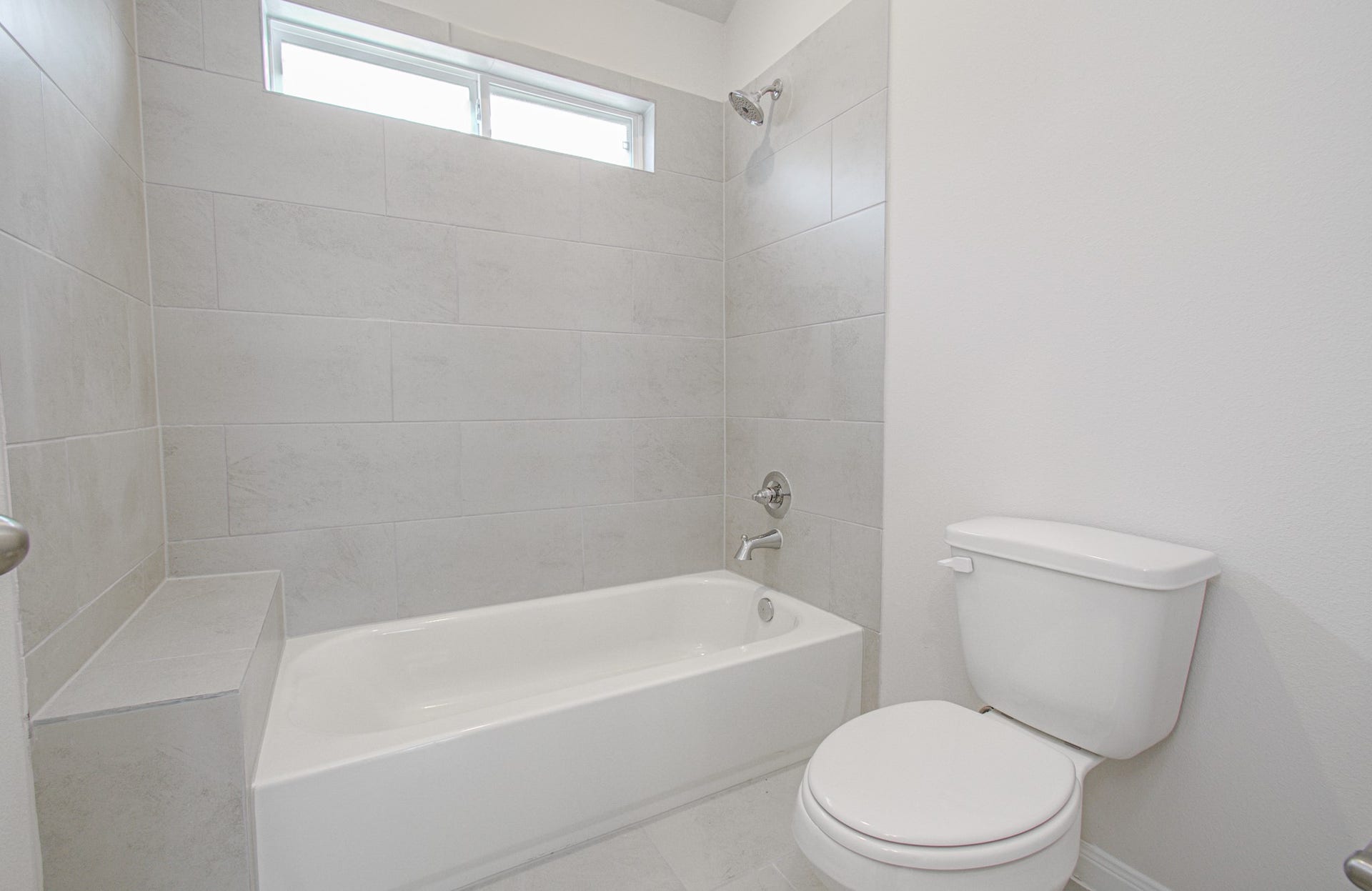14210 Aston Pine Drive, Houston, TX 77032 Bright and modern bathroom featuring a sleek bathtub with overhead shower, elegant tile work, and ample natural light. Please Note this is a different home/floorplan in the community.