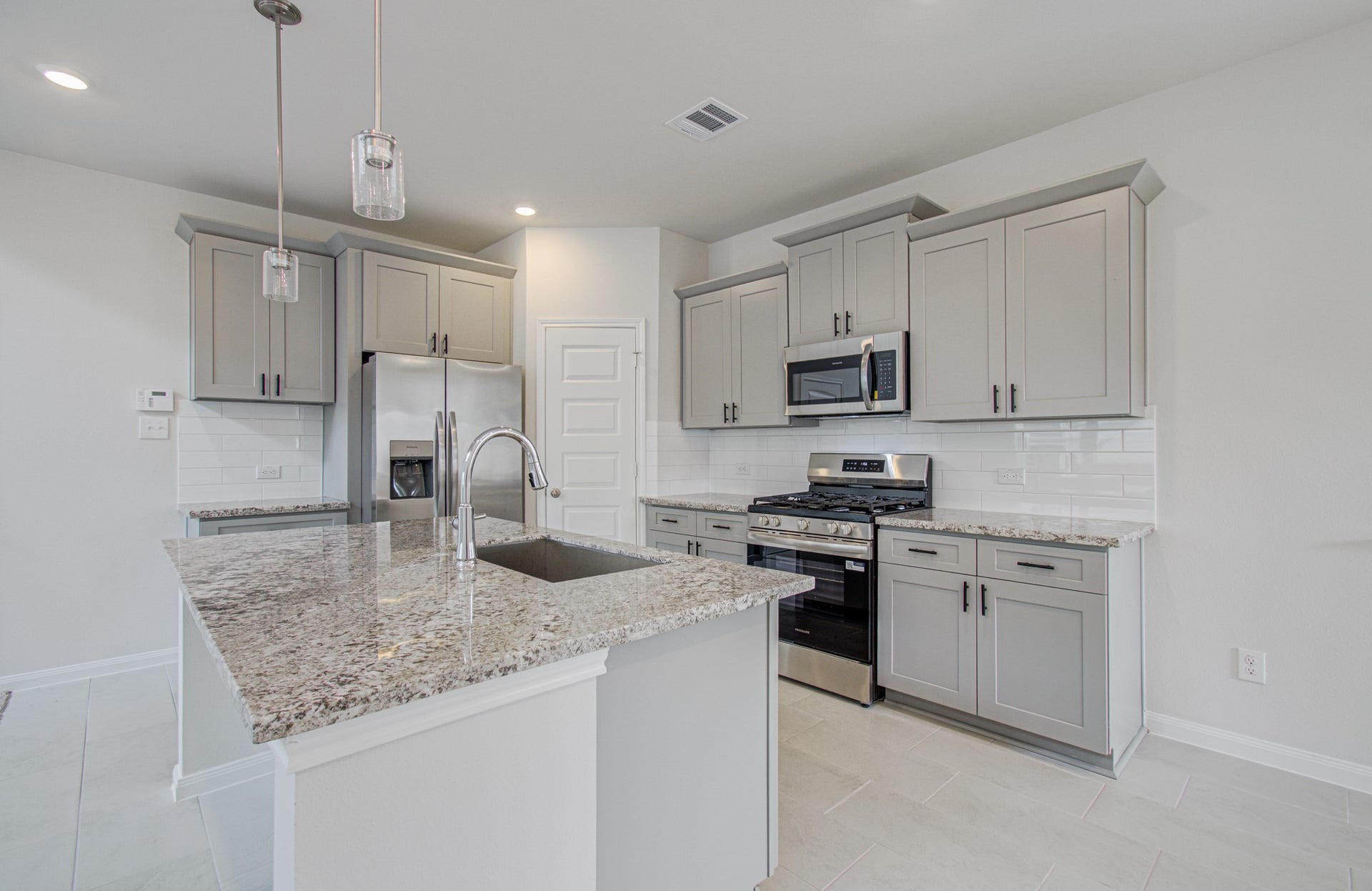 14210 Aston Pine Drive, Houston, TX 77032 Modern kitchen with sleek granite countertops, stainless steel appliances, and elegant gray cabinetry, offering a stylish and functional space. Please Note this is a different home/floorplan in the community.