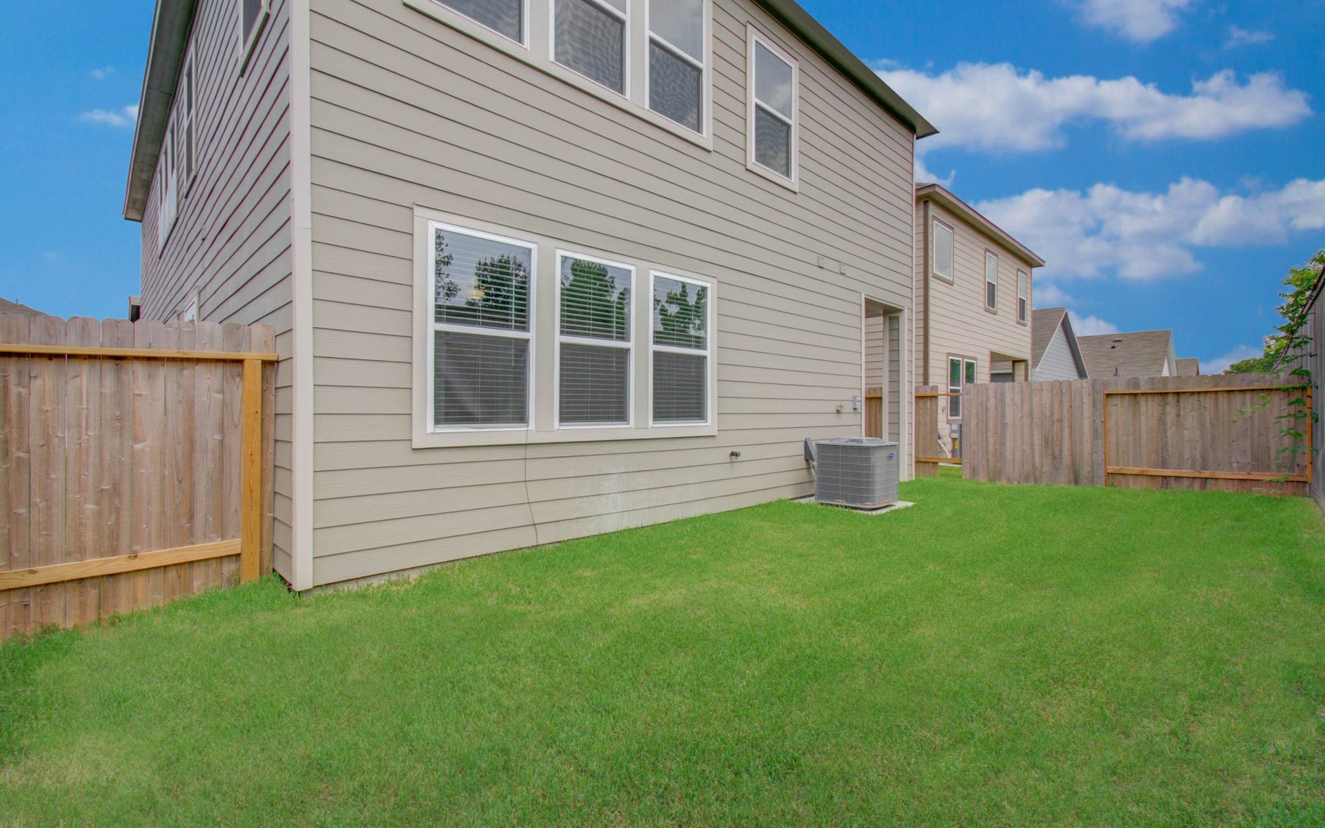 14210 Aston Pine Drive, Houston, TX 77032 Spacious backyard with well-maintained lawn, privacy fencing, and exterior access to the house, perfect for outdoor activities. Please Note this is a different home/floorplan in the community.
