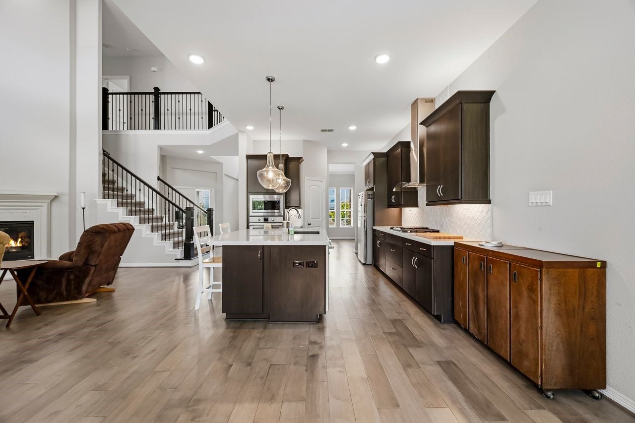 2215 Hermina Radler Drive, Richmond, TX 77469 A secondary perspective from the sunlit breakfast bay highlights the seamless flow between the kitchen and living spaces. Dark wood cabinetry and stainless steel appliances provide a sophisticated contrast to the light flooring, while a generous island anchored by elegant pendant lighting serves as the heart of the home. Modern, warm, and perfectly balanced.