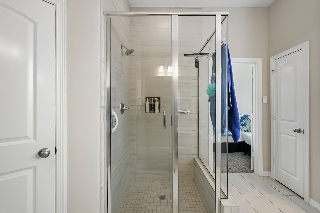 2215 Hermina Radler Drive, Richmond, TX 77469 A sophisticated primary ensuite featuring a seamless glass shower enclosure, complemented by floor-to-ceiling tiling and refined fixtures in a timeless neutral finish.