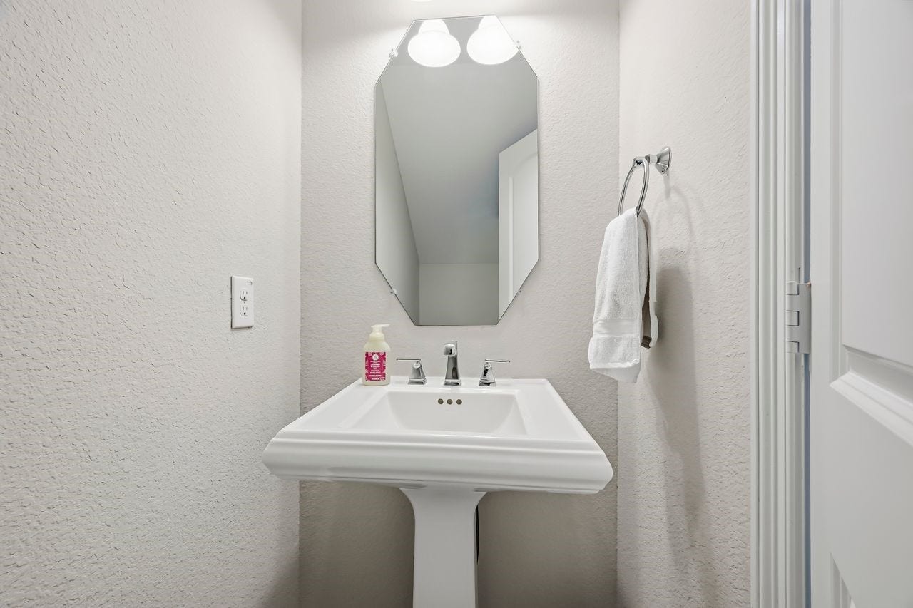 2215 Hermina Radler Drive, Richmond, TX 77469 Sophisticated and serene, this guest powder room features a classic white porcelain pedestal sink complemented by neutral tones, refined wall-mounted lighting, and a polished mirror.