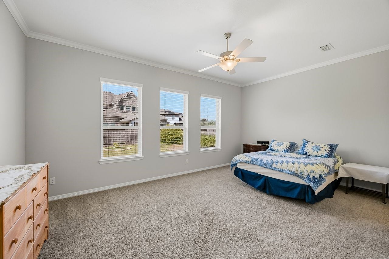 2215 Hermina Radler Drive, Richmond, TX 77469 Step into the primary retreat, where elegant crown molding and expansive windows frame a serene view of the lushly landscaped grounds. This spacious sanctuary is complete with a cooling ceiling fan and an abundance of natural light.