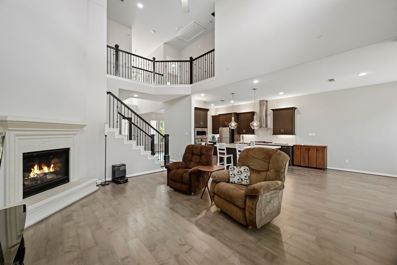 2215 Hermina Radler Drive, Richmond, TX 77469 This sophisticated open-concept space seamlessly integrates the living area, breakfast nook, and kitchen, anchored by a contemporary fireplace and a stylish staircase leading to the upper catwalk. Neutral finishes and bold dark accents complement the rich wood flooring, creating a cohesive and inviting vista from the primary retreat entrance.