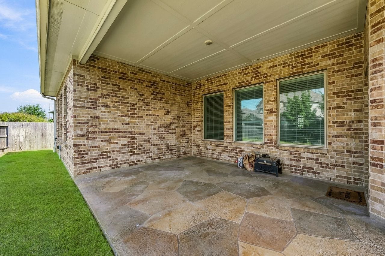 2215 Hermina Radler Drive, Richmond, TX 77469 This expansive covered patio features elegant stone-patterned flooring and offers a serene vantage point over the meticulously landscaped grounds and tranquil water feature.