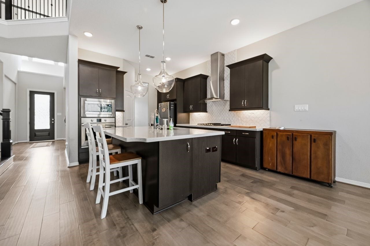 2215 Hermina Radler Drive, Richmond, TX 77469 Looking through to the entryway, this contemporary kitchen makes a sophisticated statement with its rich, dark cabinetry and sleek tile backsplash. The space is thoughtfully designed with under-cabinet lighting and a suite of high-end stainless steel appliances, including a gas cooktop and built-in microwave.