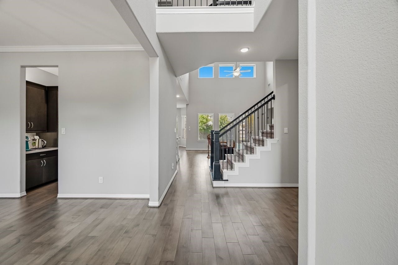 2215 Hermina Radler Drive, Richmond, TX 77469 Experience an immediate sense of scale and light in this striking open-concept entryway. Soaring ceilings and a sophisticated staircase anchor the space, while expansive windows bathe the crisp palette and warm wood flooring in natural radiance. The layout flows effortlessly, offering a seamless transition toward the kitchen and breakfast area or providing convenient access to the private study and utility wing.