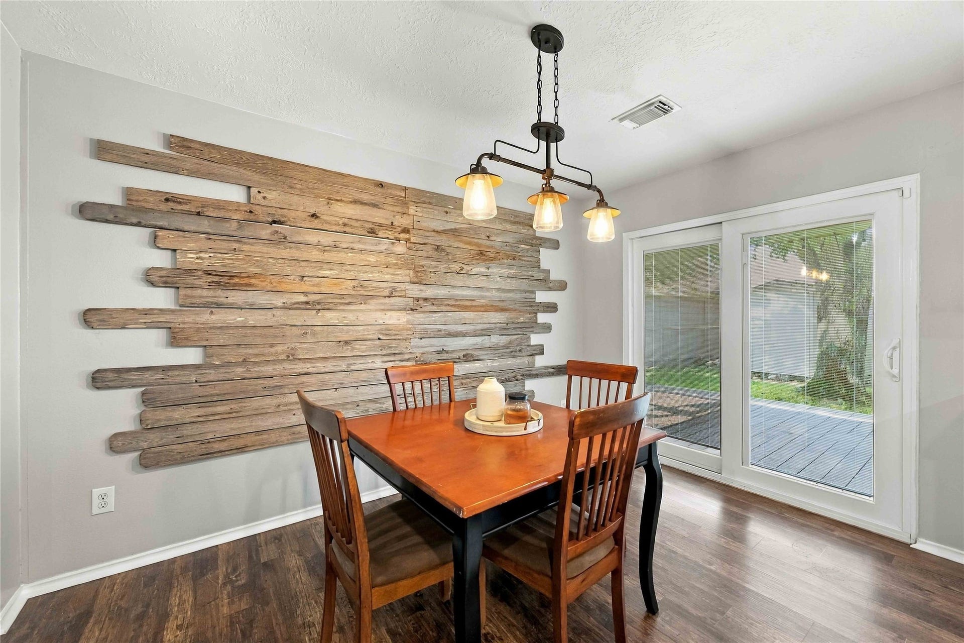 Dining area accented by a distinctive reclaimed-wood feature wall, statement lighting, and sliding glass doors opening to the outdoor living space.