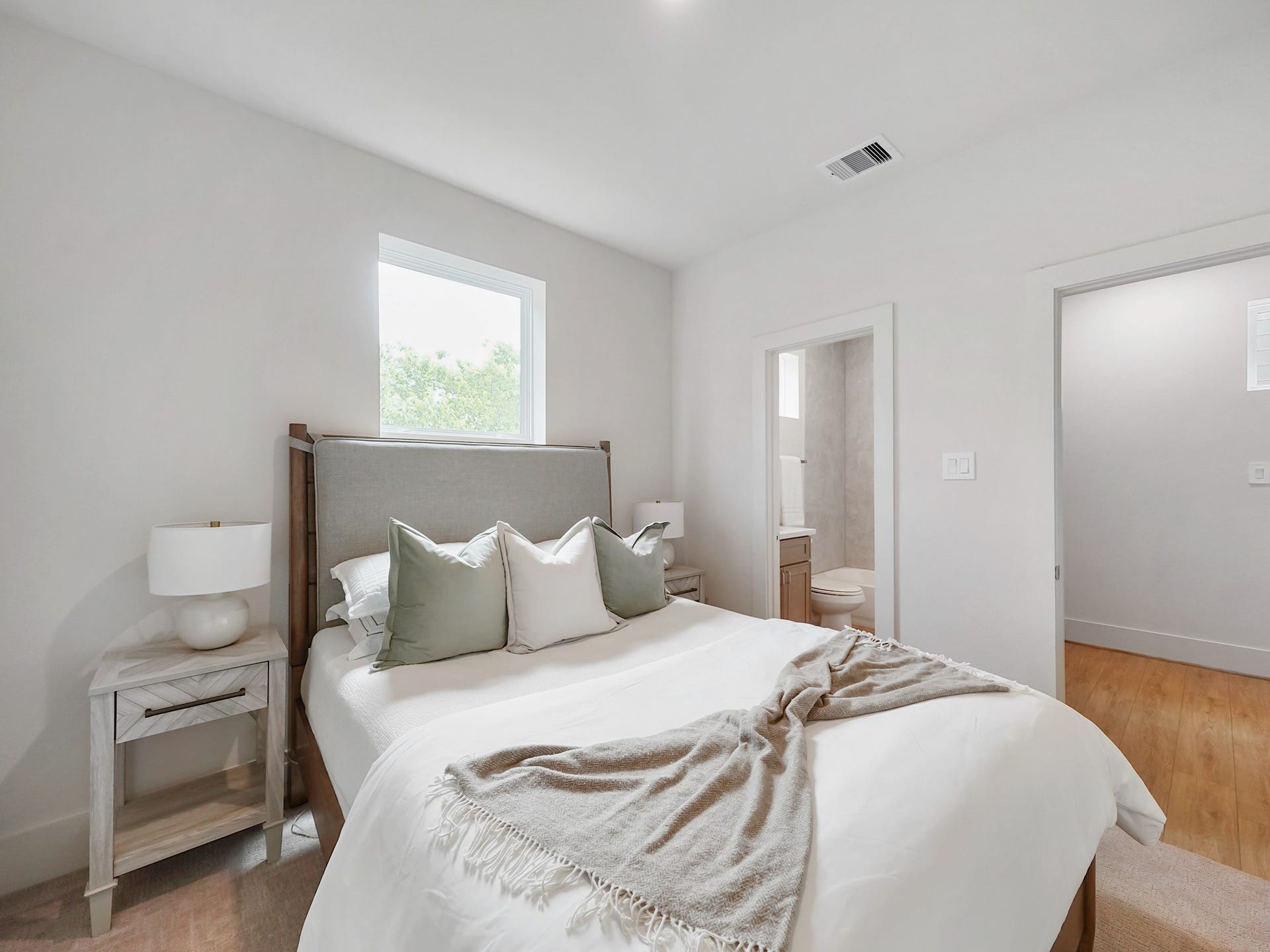 This inviting second bedroom features a bright, airy ambiance with a cozy bed, modern decor, and an en-suite bathroom, perfect for relaxation and comfort.