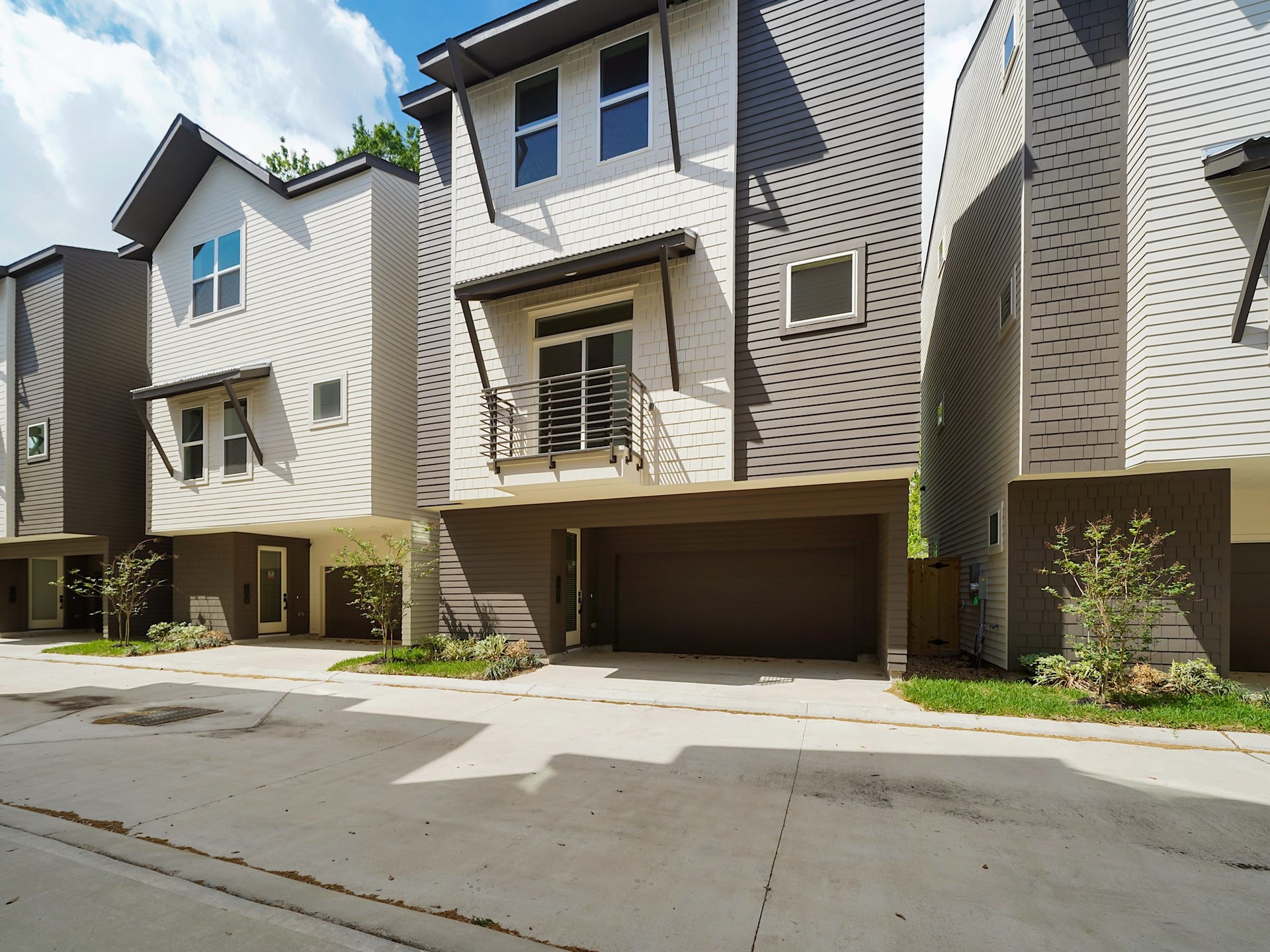 Modern three-story townhouse with a two-car garage, sleek exterior design, and a small front yard, situated in a row of similar homes.