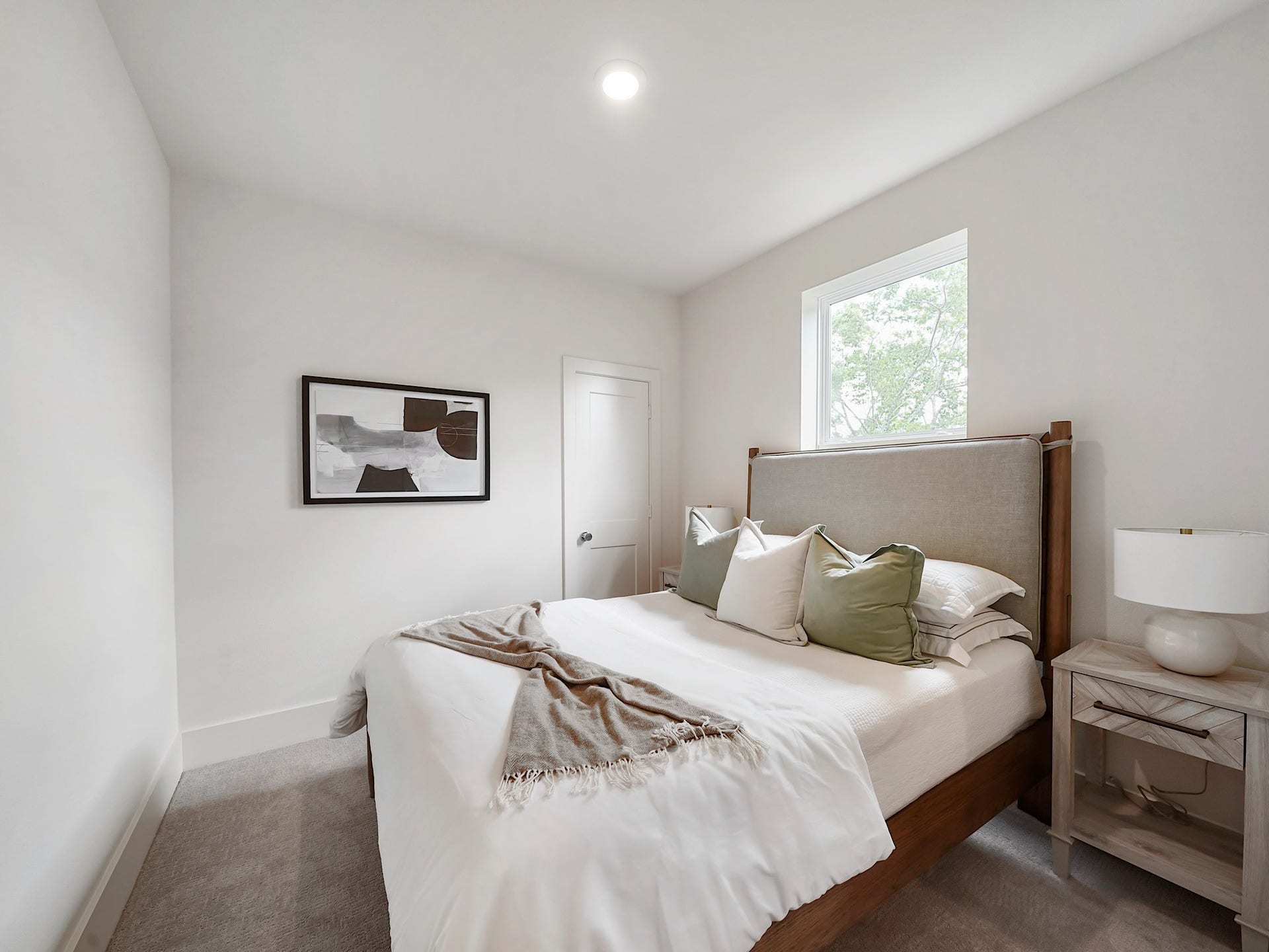 This inviting second bedroom offers a serene retreat with its soft, neutral palette, cozy bedding, and ample natural light, perfect for relaxation or guests.