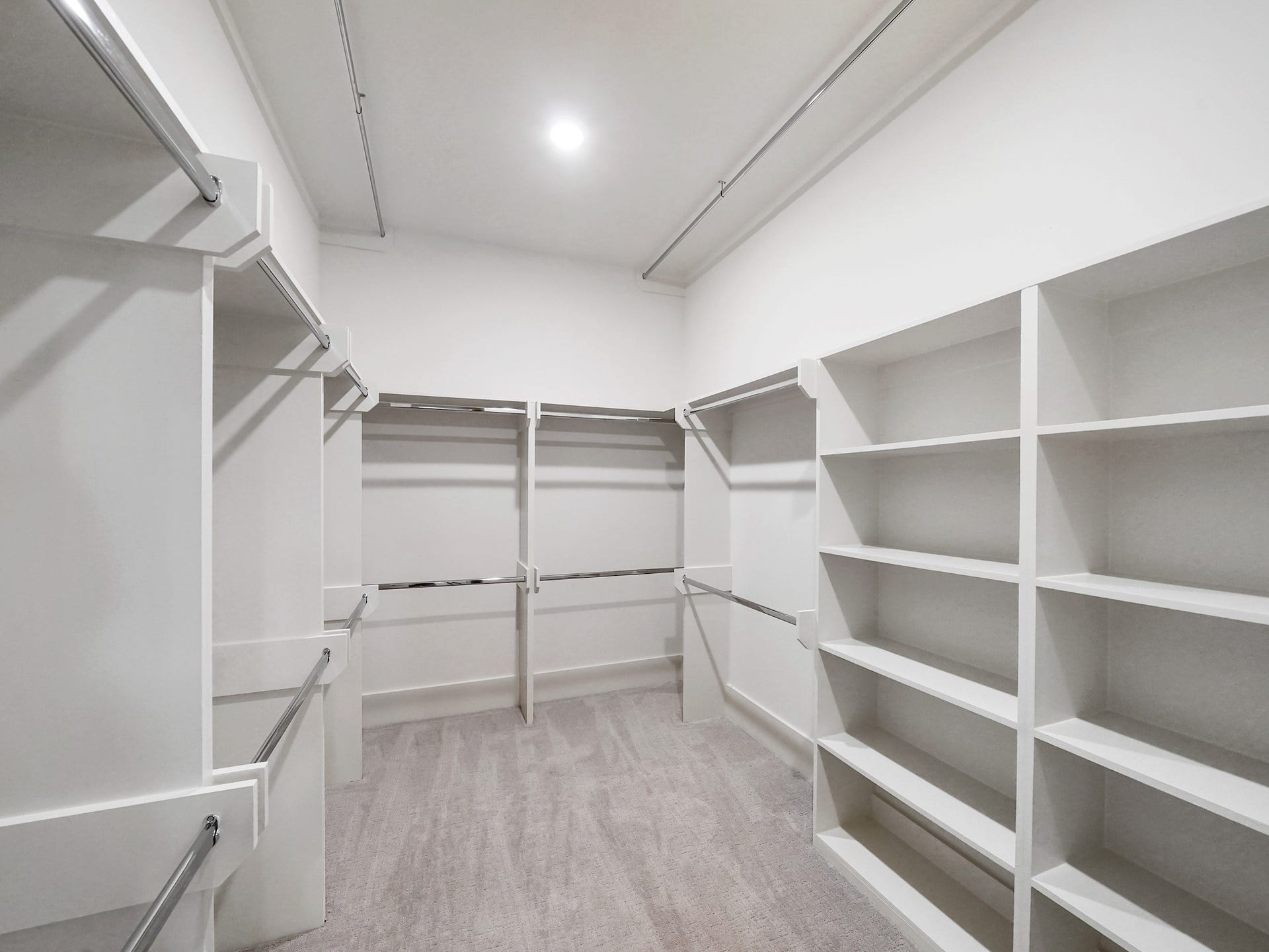 Discover a spacious walk-in primary closet featuring elegant built-in shelves, perfect for organized luxury living.