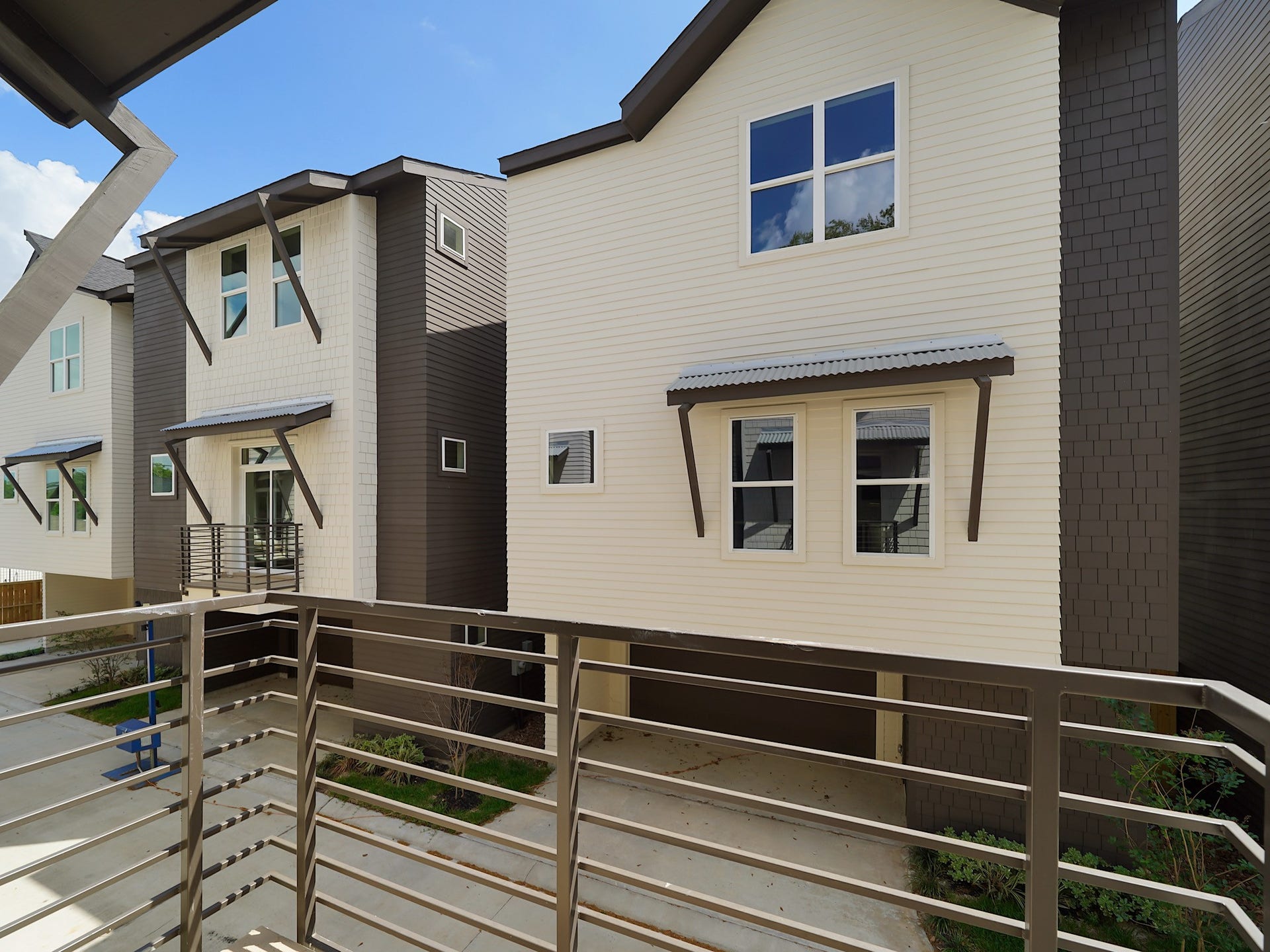 Modern townhouses with sleek, two-toned exteriors and large windows. The view includes a shared driveway and minimal landscaping, providing a clean and contemporary look.