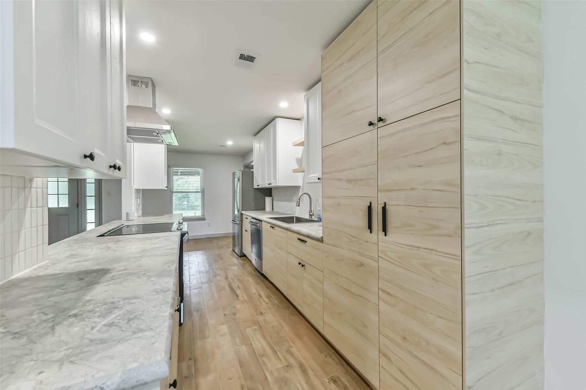 Kitchen features modern cabinetry with a mix of light wood and white finishes, complemented by sleek countertops. It has stainless steel appliances, ample storage, and hardwood flooring, creating a bright and functional space.