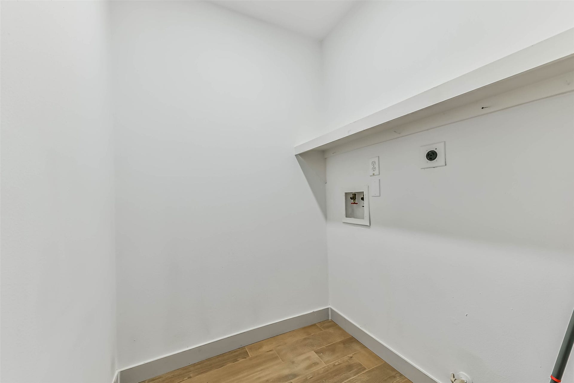 A compact laundry room with washer and dryer hookups, featuring white walls and light wood flooring.