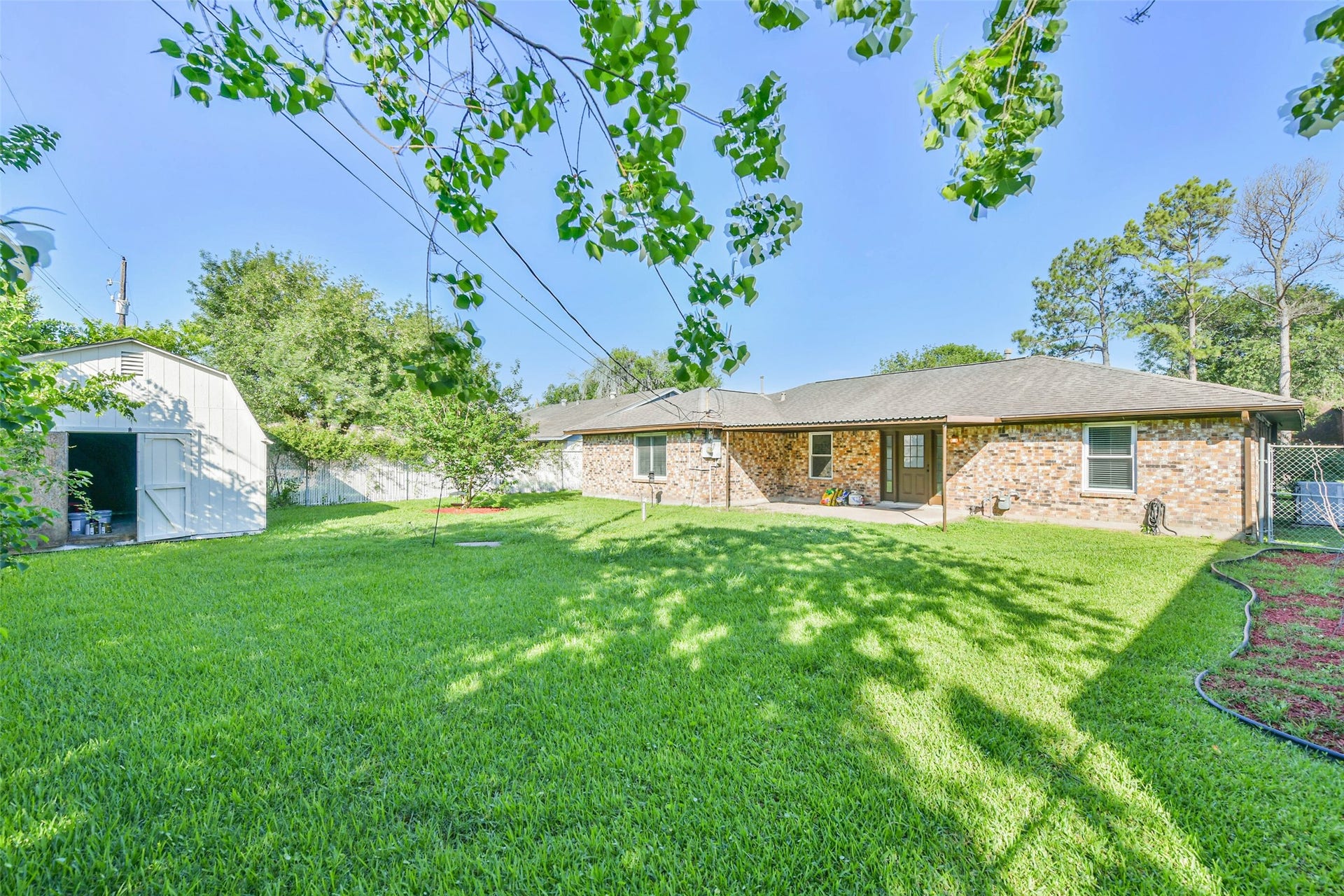 Spacious backyard with lush green lawn, a brick exterior home, and a large storage shed. Ideal for outdoor activities and storage needs.