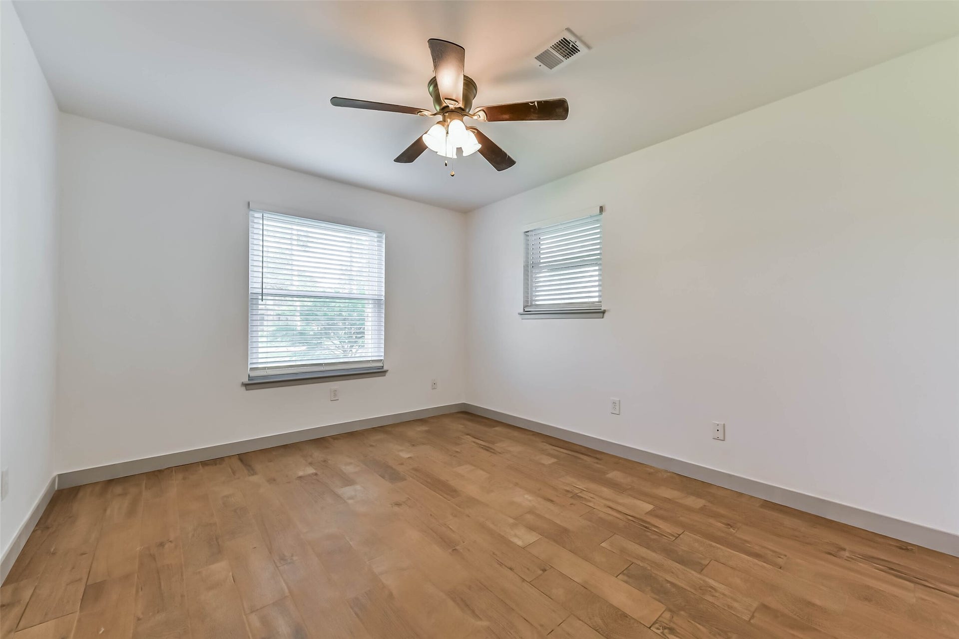 Bedroom features hardwood floors, neutral walls, and a ceiling fan. Two windows provide natural light.