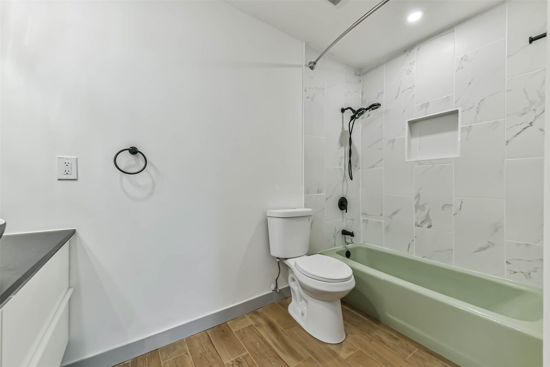 Bathroom features a modern design with a light green bathtub, white marble tiled shower, and wood-style flooring.