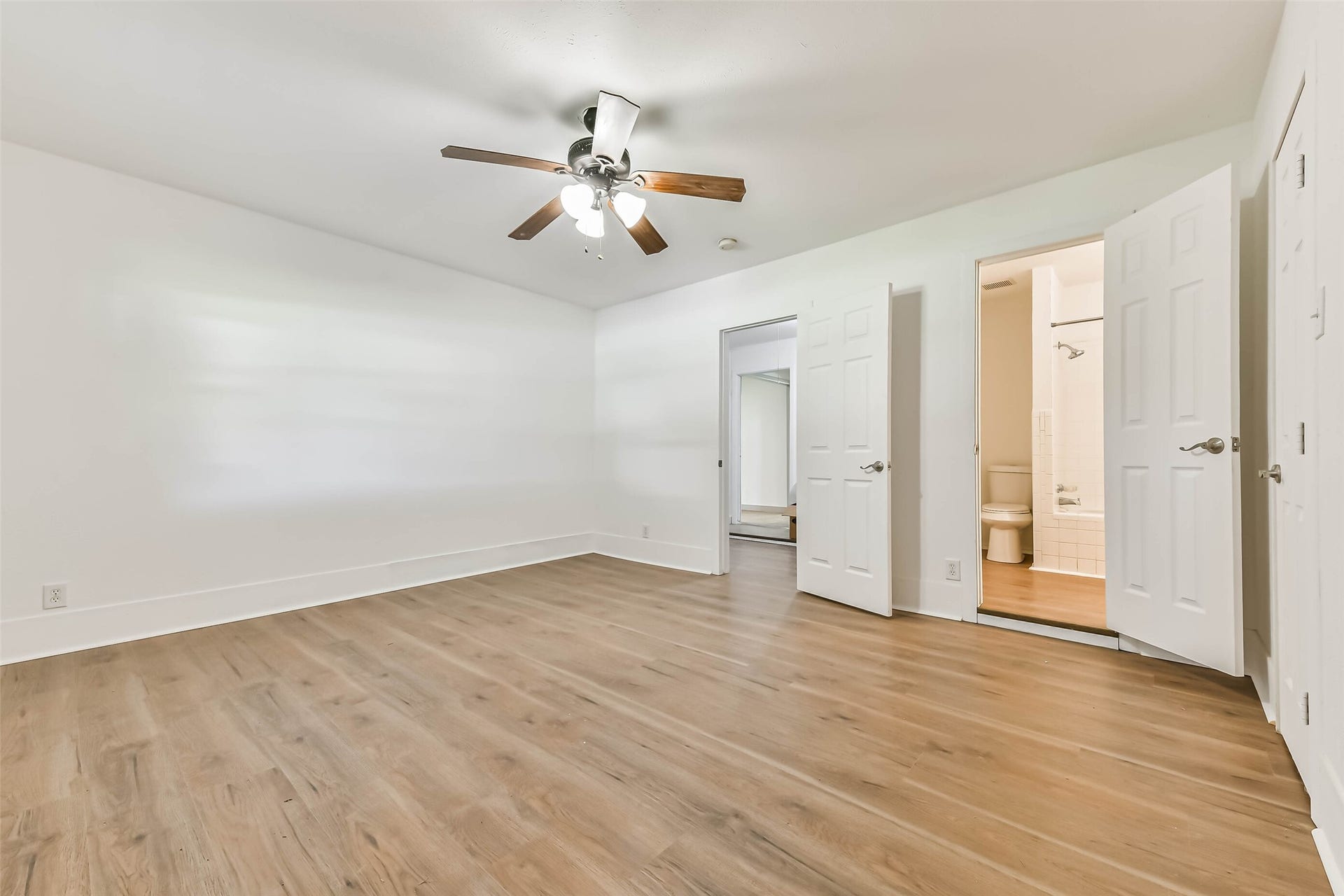 Bedroom with wood flooring, a ceiling fan, and neutral walls. It features access to an en-suite bathroom.