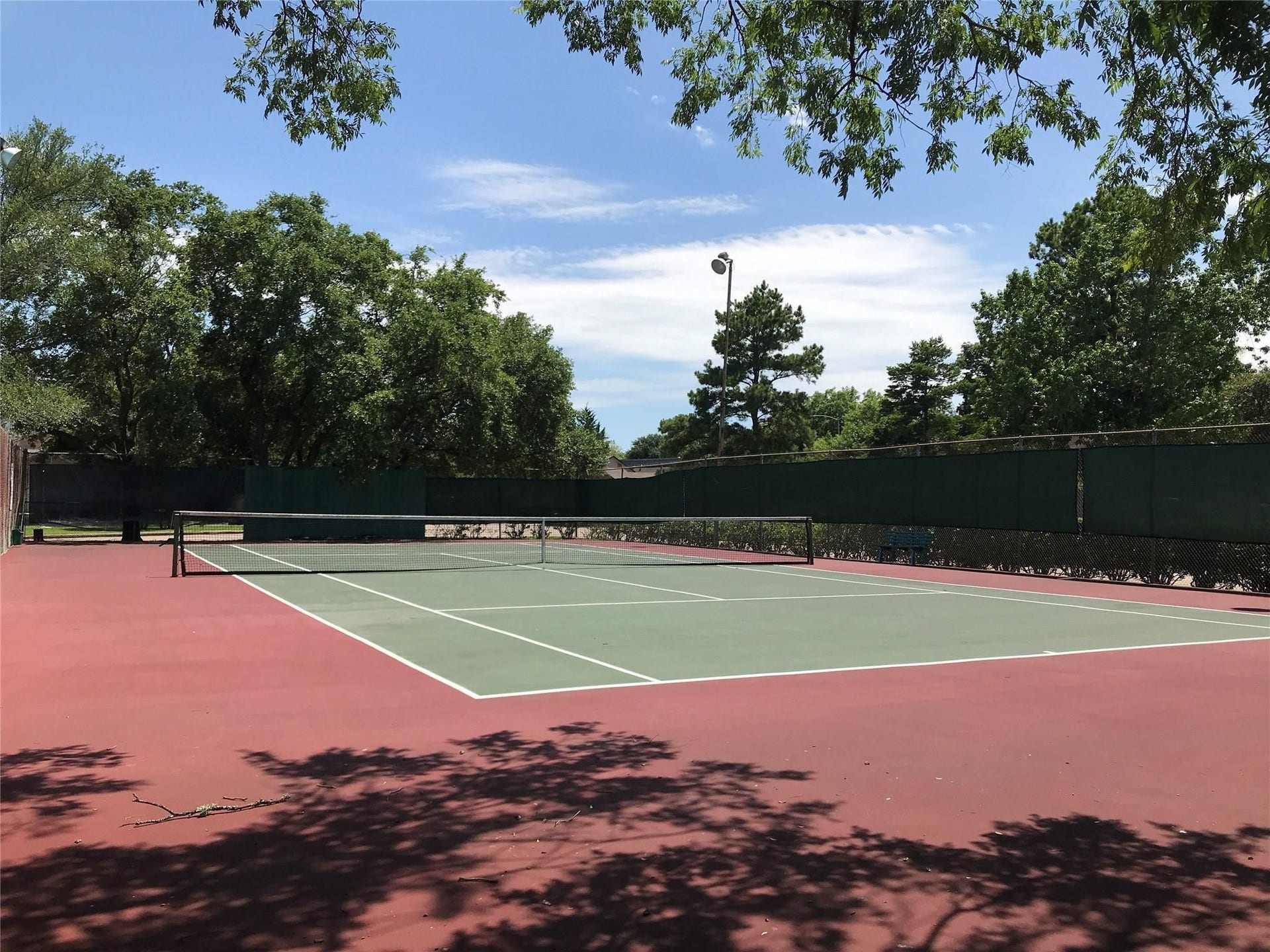 12719 Hollandale Drive, Houston, TX 77082 Westpark Village Tennis court is surrounded by fencing and mature trees, providing an outdoor space for recreational activities.