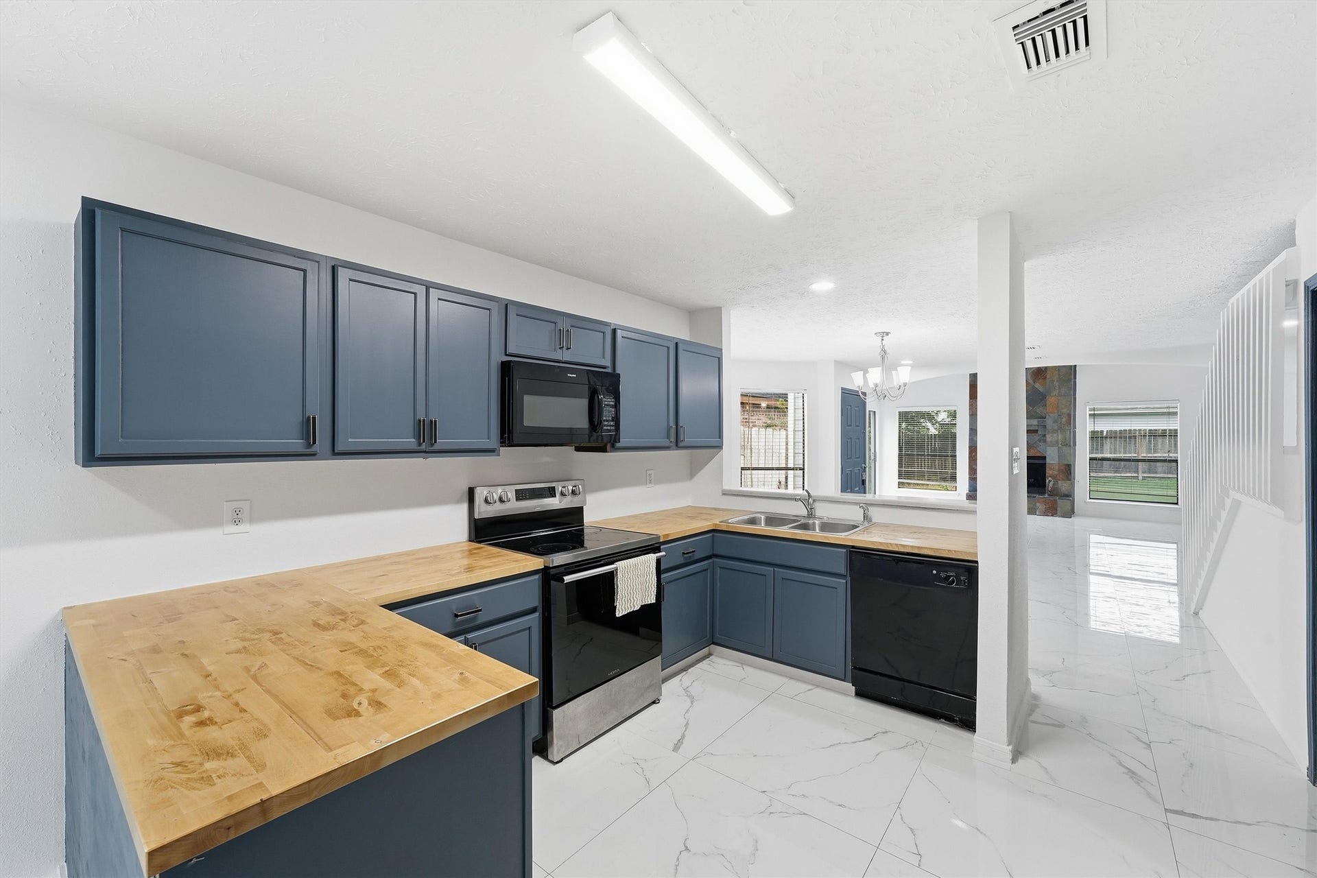 12719 Hollandale Drive, Houston, TX 77082 Kitchen brings together blue cabinetry, wood-look countertops, a breakfast bar, and easy access to the dining areas.