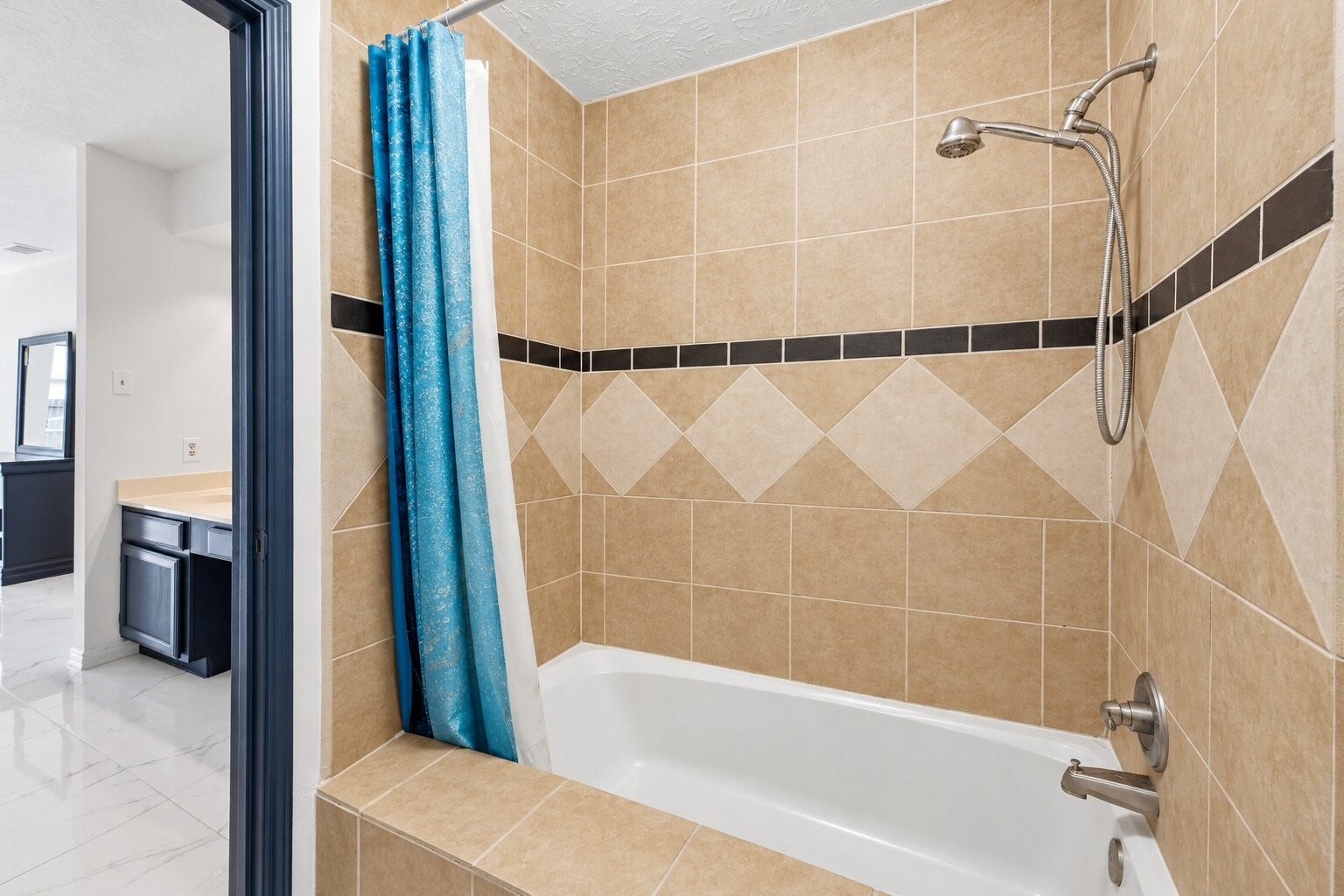 12719 Hollandale Drive, Houston, TX 77082 Primary bath includes a double-sink vanity, wide mirror, and tub-shower combination surrounded by decorative tile walls.