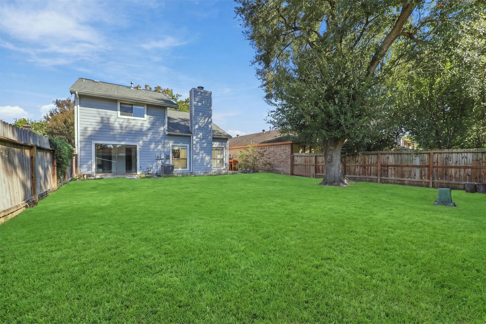 12719 Hollandale Drive, Houston, TX 77082 Backyard welcomes outdoor activities on a spacious green lawn surrounded by a wood fence and mature trees.