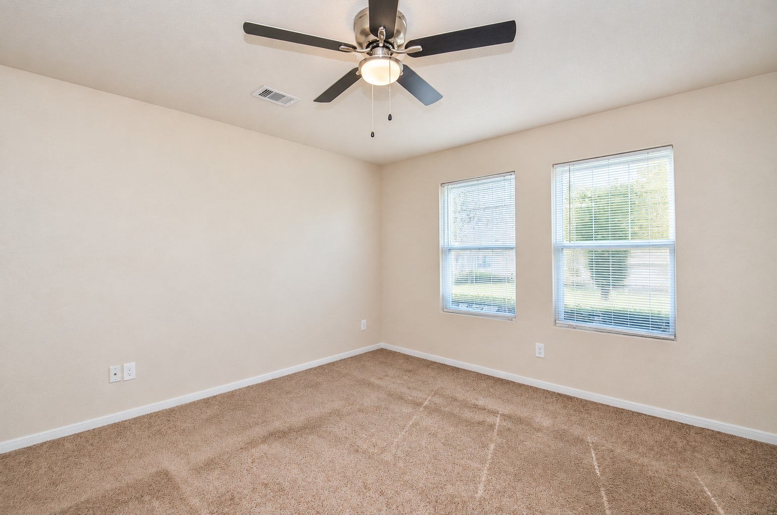 5031 Grove Square Court, Katy, TX 77449 First-floor primary bedroom featuring neutral carpeting, a ceiling fan and two windows providing abundant natural light.