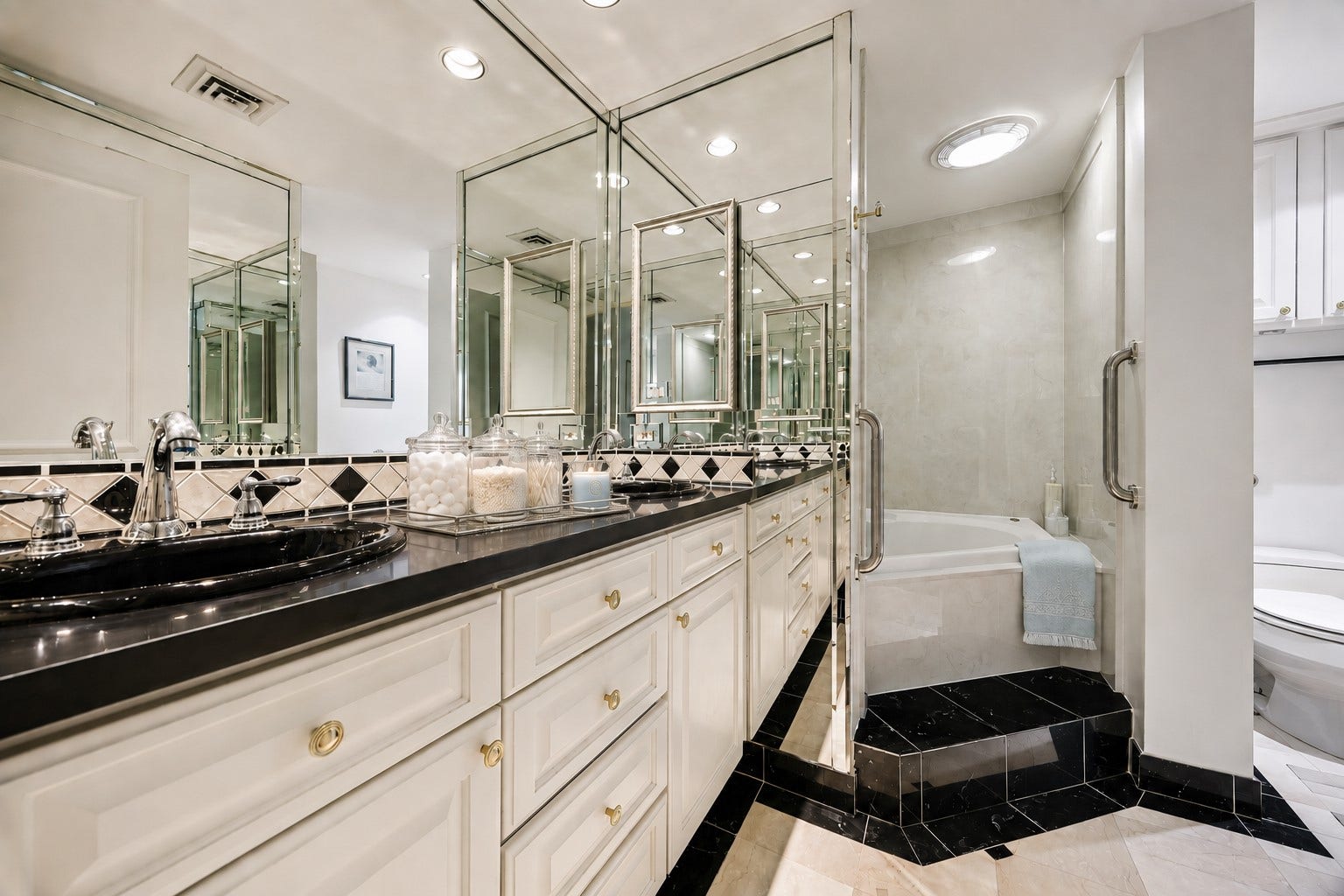 Luxurious primary bathroom featuring dual-sink comfort-height vanity topped with premium granite counters and custom designed framed mirrors. For a quiet evening and after a long day, enjoy a spa-like retreat with the large deep soaking tub separated by a water closet privacy partition.