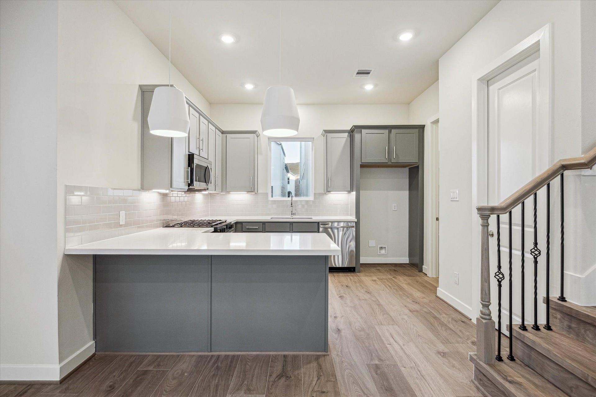 Kitchen featuring a large peninsula, gray cabinetry, white countertops, subway tile backsplash, pendant lighting, stainless steel appliances, and an open connection to the main living area.