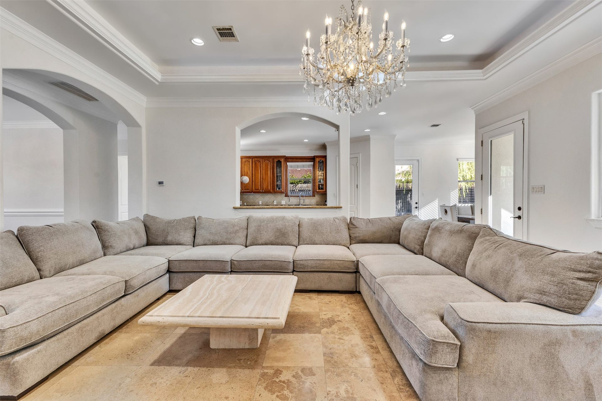 8606 Argentina Street, Houston, TX 77040 Elegant living room featuring high tray ceilings framed by intricate crown molding, a stunning chandelier with a decorative ceiling medallion, and graceful arched openings. Abundant natural light enhances the spacious, inviting atmosphere.