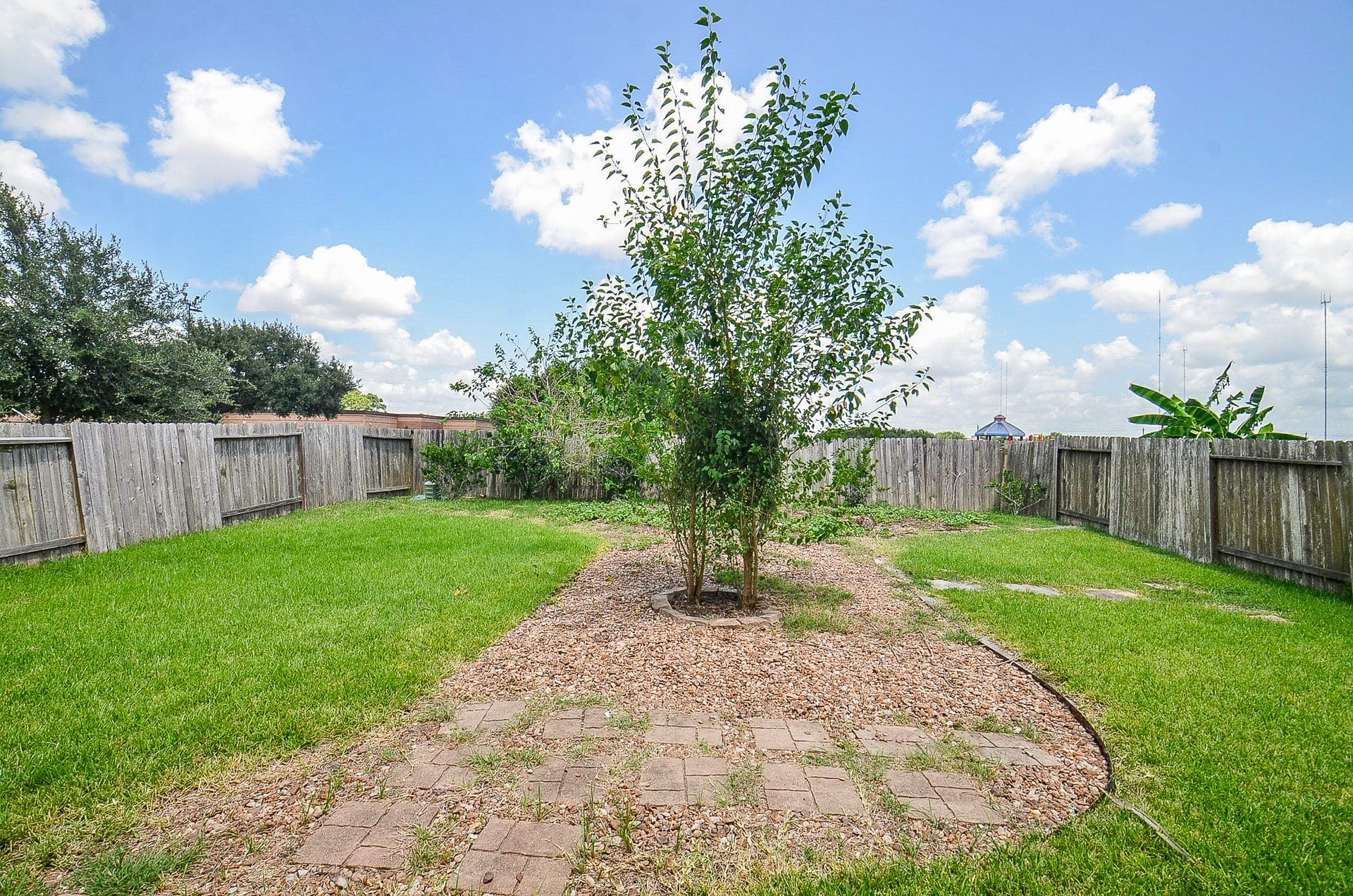 2539 Bedrock Lane, Missouri City, TX 77489 Spacious backyard with lush green grass, a central tree, and a charming stone pathway, all enclosed by a wooden fence for privacy.