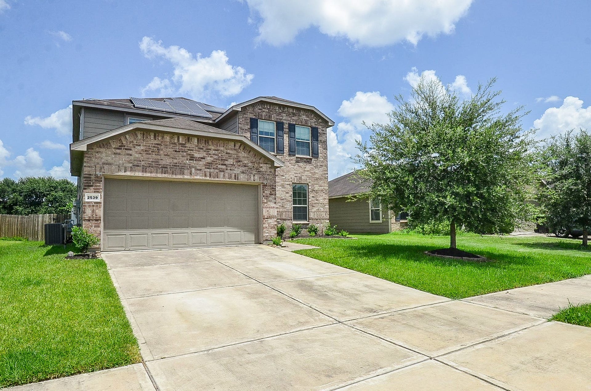 2539 Bedrock Lane, Missouri City, TX 77489 Two-story brick home with a spacious driveway and attached garage, surrounded by lush green landscaping.