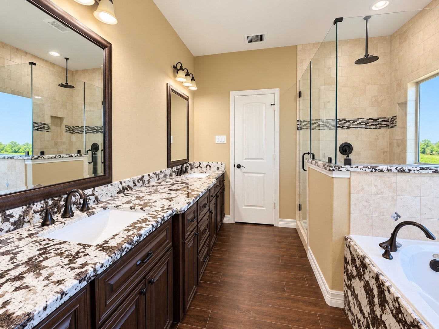 8999 Water Point Drive, Beach City, TX 77523 Elegant bathroom featuring dual sinks with striking granite countertops, a spacious glass-enclosed shower, and a luxurious soaking tub, all enhanced by warm wood cabinetry and modern fixtures.