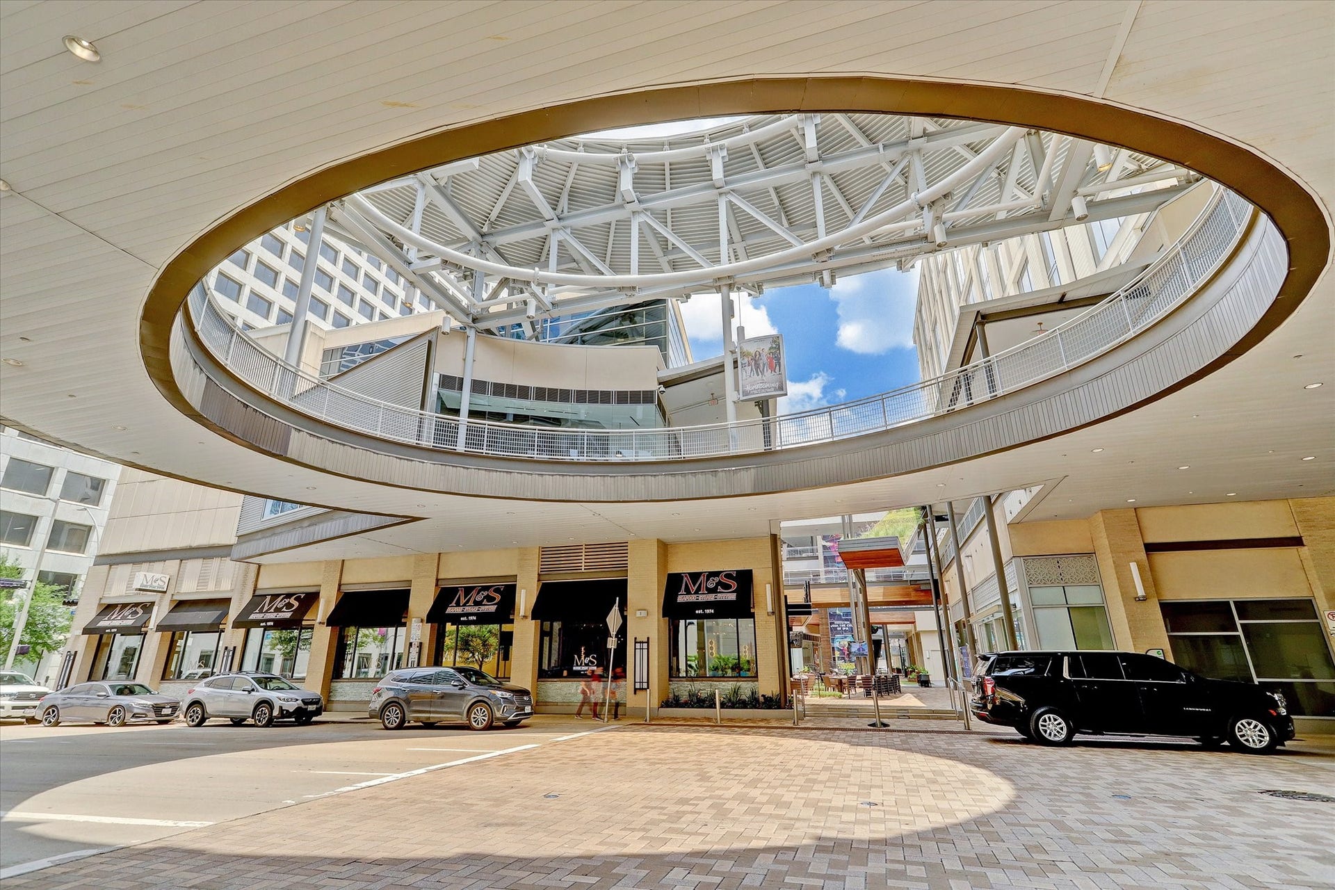 1111 Caroline Street, #2606, Houston, TX 77010 Houston Pavilions / GreenStreet complex, a vibrant downtown destination blending shopping, dining, fitness, and entertainment. Visible here is McCormick & Schmicks Seafood & Steaks (M&S), one of the anchor restaurants. Within the same development, visitors can enjoy LA Fitness, House of Blues Houston, stylish retail shops, and outdoor gathering spaces. The modern open-air design with steel trusses and circular cutouts above creates a dynamic, urban feel while connecting to the surrounding businesses.