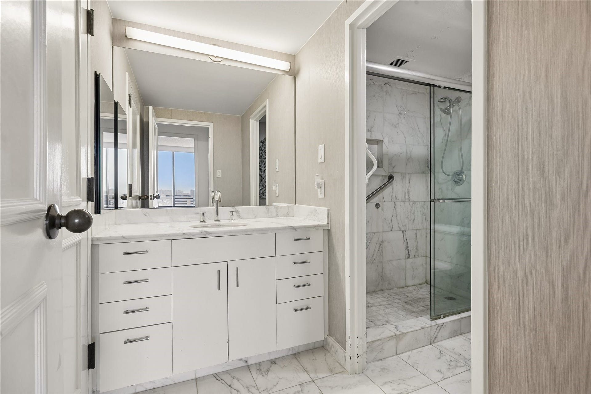 1111 Caroline Street, #2606, Houston, TX 77010 Drawer storage and a long vanity counter keep daily essentials organized. A large mirror and glass enclosed shower with light veined finishes complement the bathroom's practical layout.