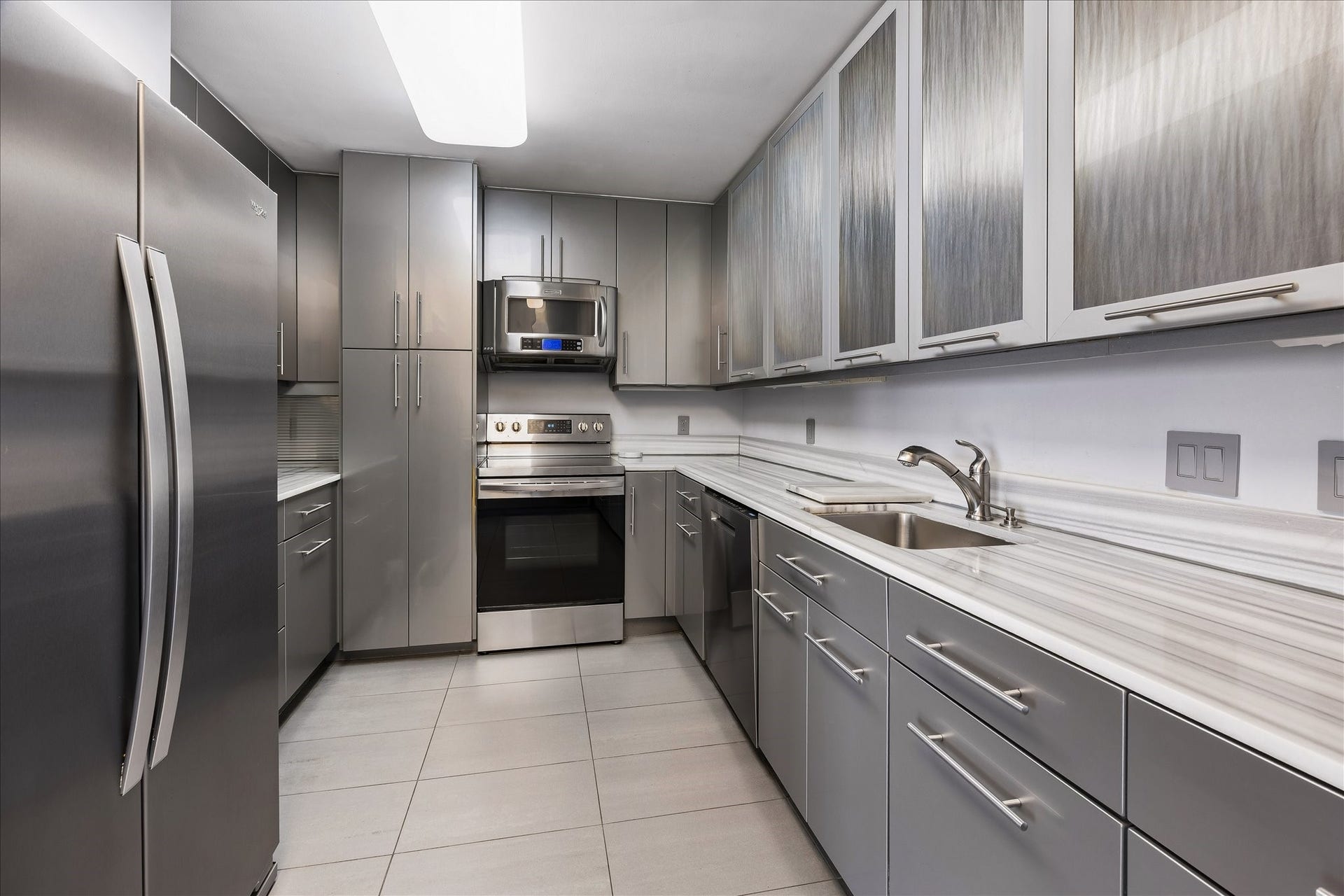 1111 Caroline Street, #2606, Houston, TX 77010 Gray cabinetry, textured glass upper doors and long counters define the galley kitchen. Storage and preparation areas line both sides, with stainless finish appliances supporting everyday cooking.