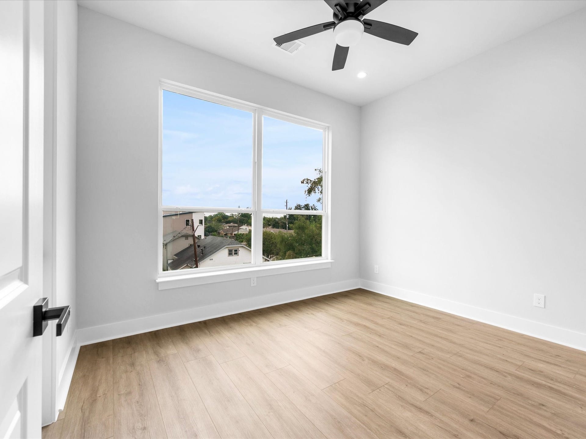 Large windows fill this secondary bedroom with natural light, highlighting the beautiful flooring and inviting design.