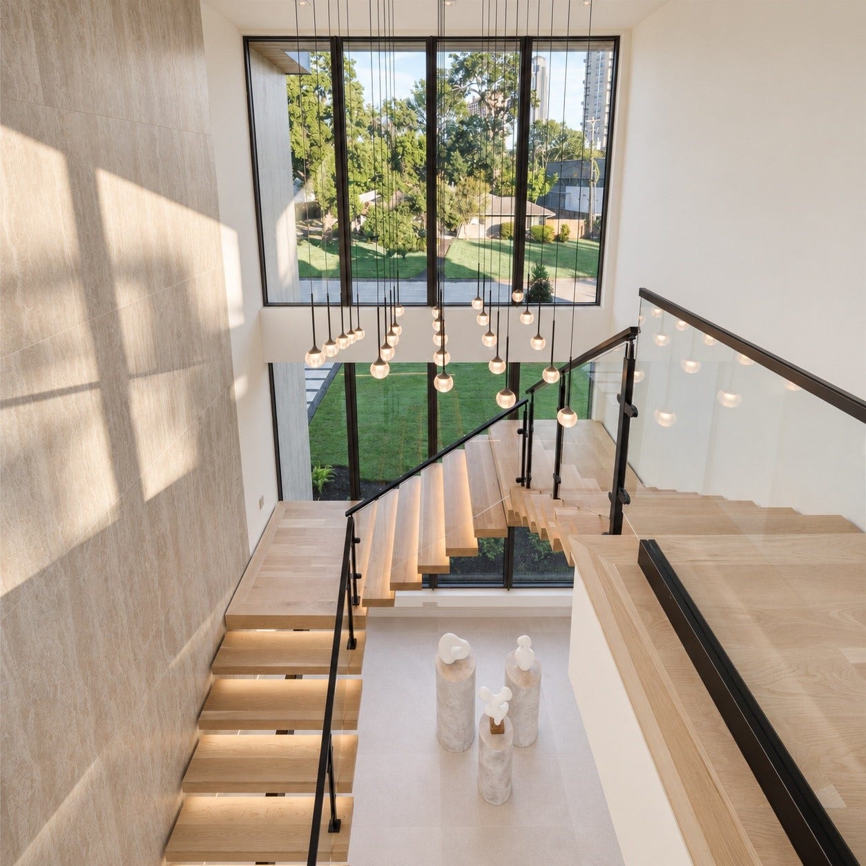 An alternate view of the dramatic staircaserevealing the artistry. Cascading pendant lights creating a striking accent to the second level. Floor-to-ceiling windows. flood the space with natural light and frame lush outdoor views, giving this a sense of openness and connection to the outdoors.